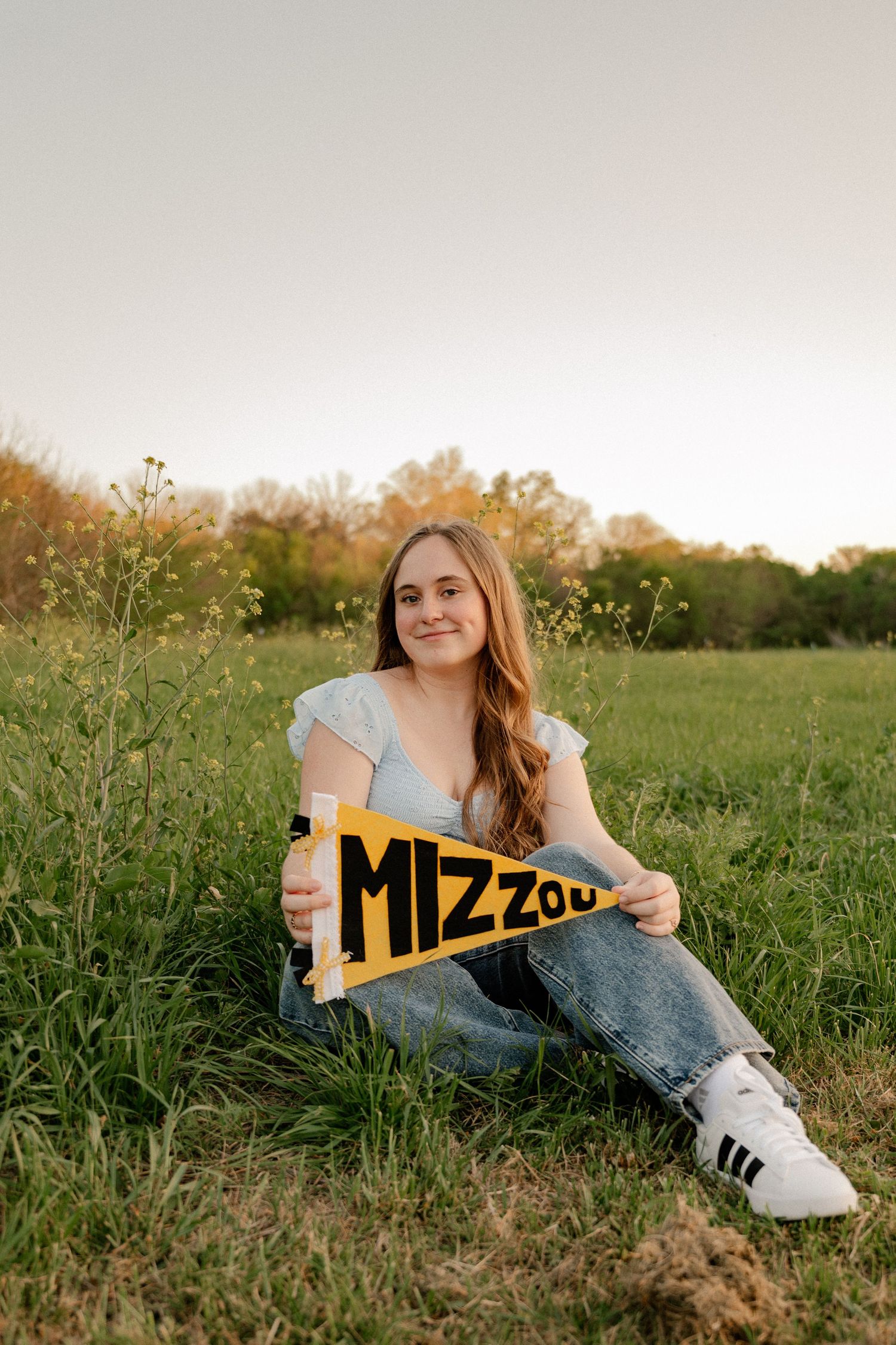 High School senior posing with a college pennant in a wildflower field for a Spring senior photo session in Richardson, Texas