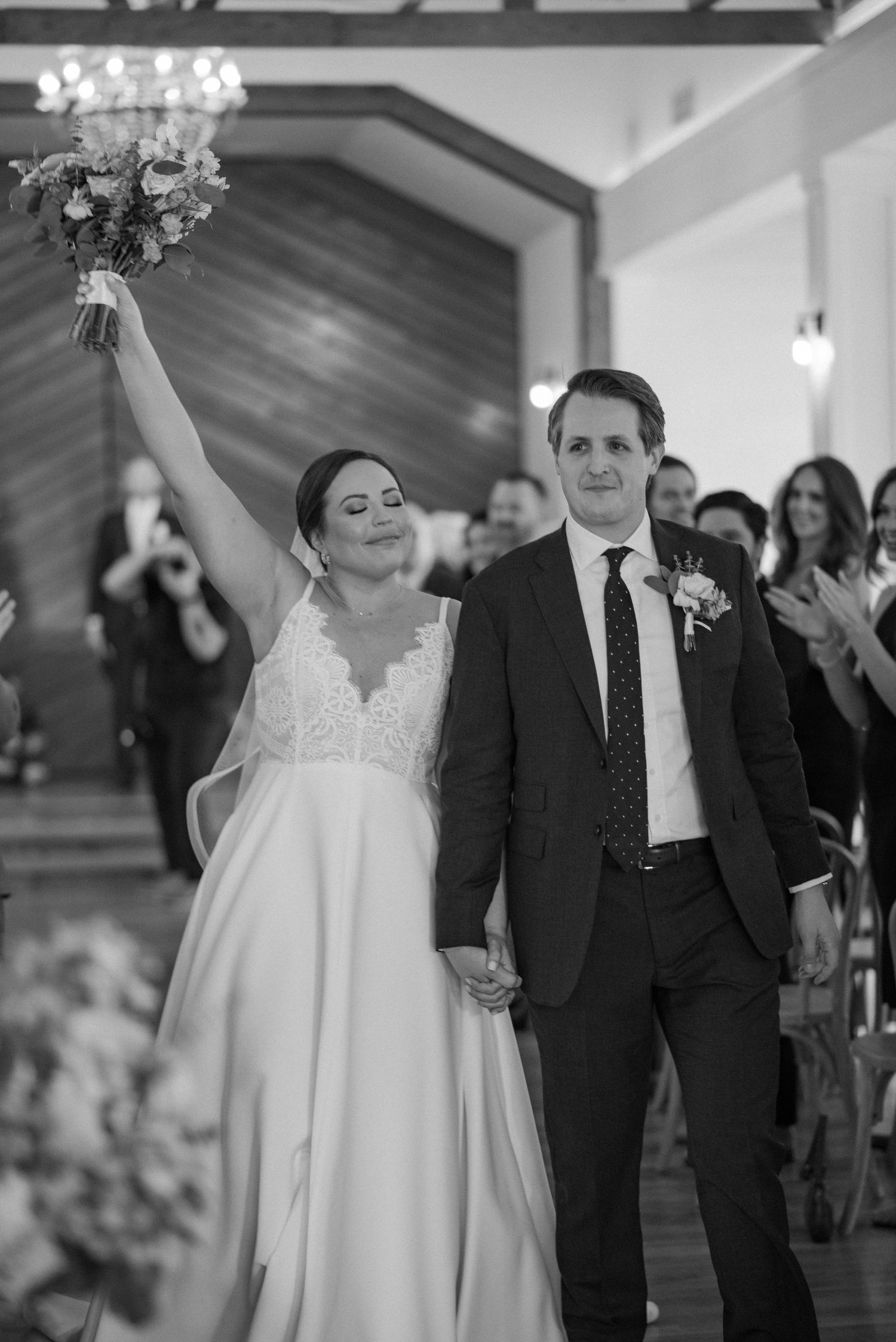 A triumphant wedding recessional moment of bride and groom in black and white with guests applauding.