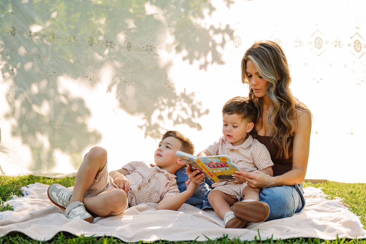 Mother reading her 2 sons a book while they sit on a blanket in the grass as the sun sets for their summer family photo session