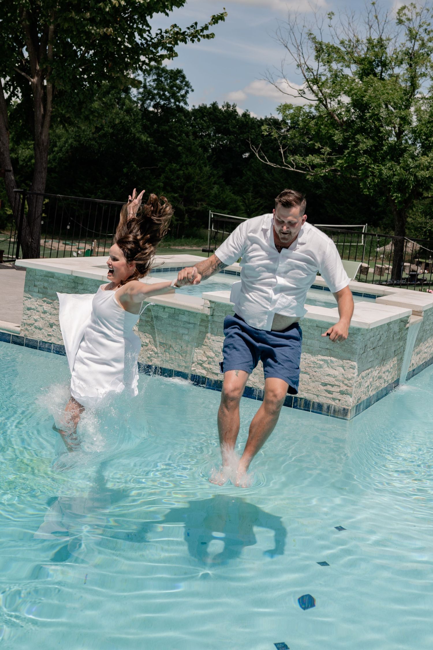 Recently married couple jumping into a swimming pool in their wedding clothes after an intimate Summer wedding ceremony in McKinney, Texas