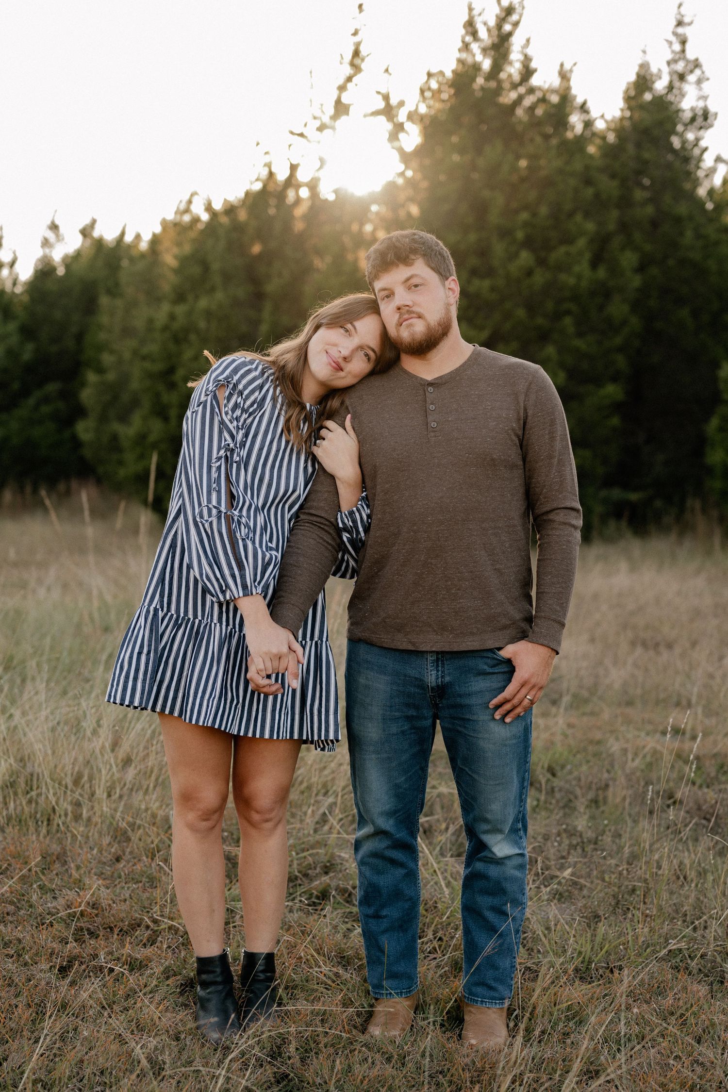 Married couple embracing during a casual fall couple session in a large tree lined field in during golden hour