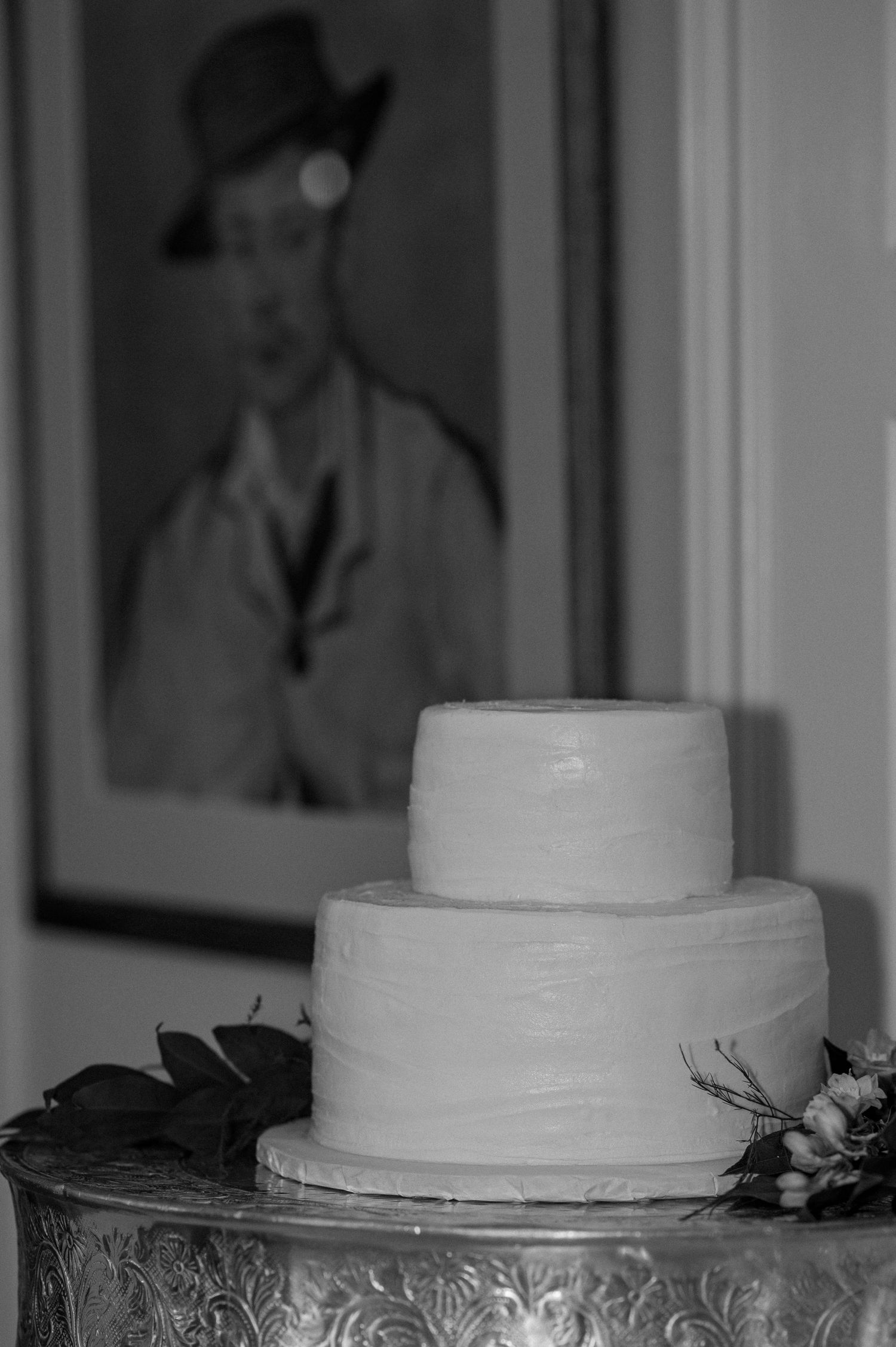 A simple two-tiered white wedding cake displayed next to a vintage portrait in black and white.