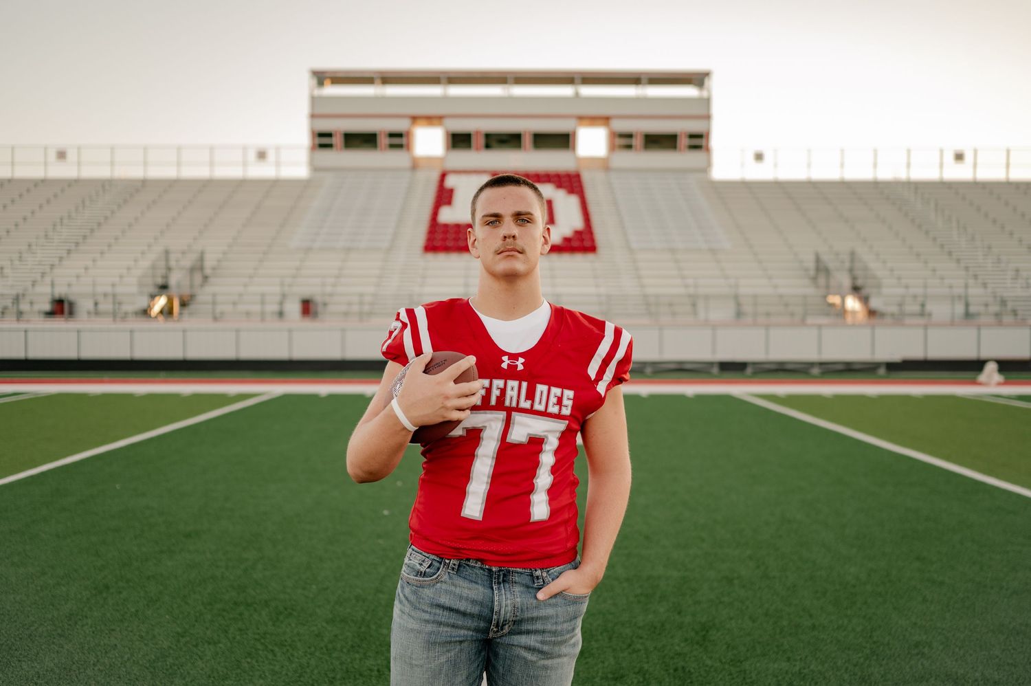 Senior boy seriously posing in a football stadium for his summer senior photo session in Lone Oak, Texas