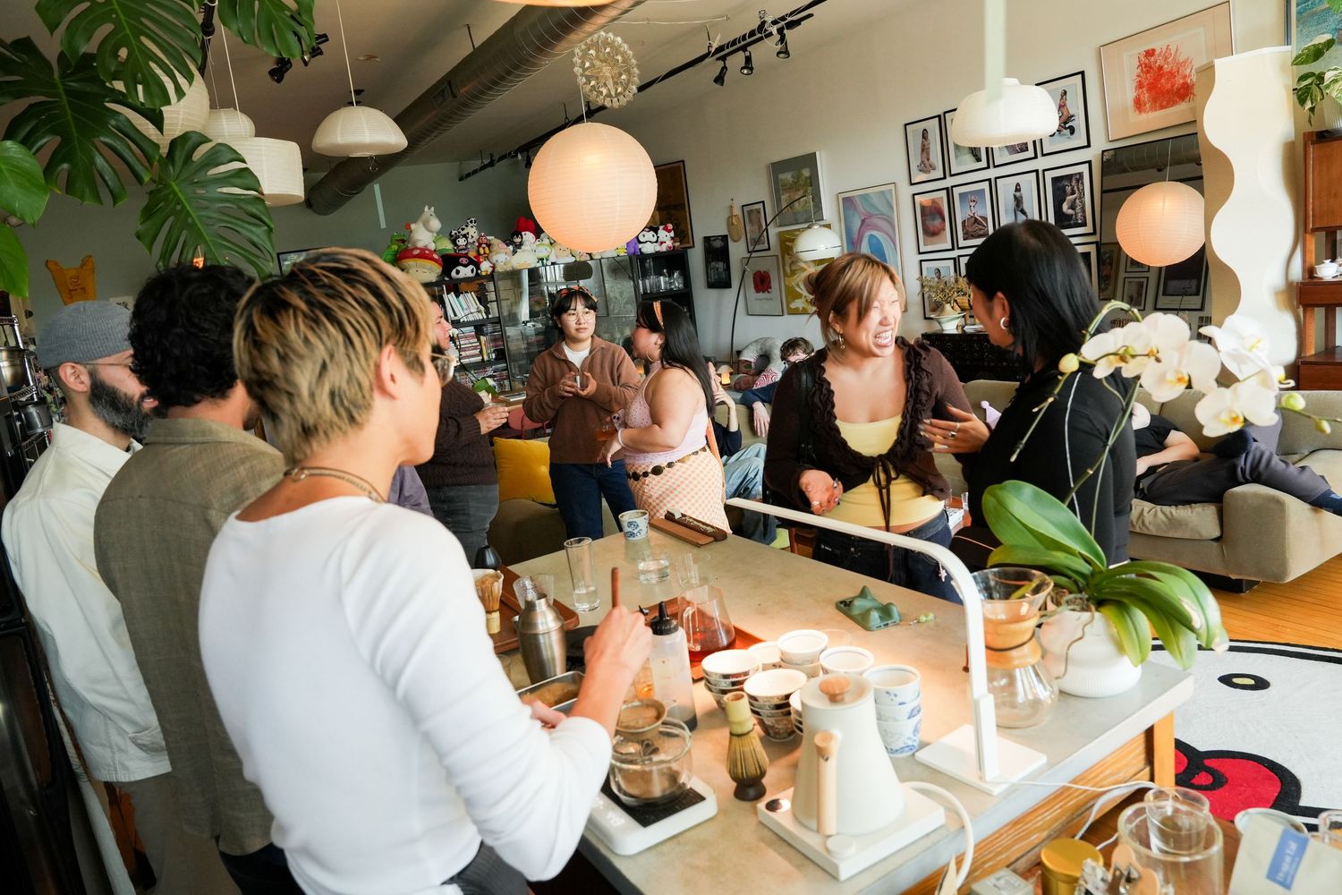 Busy cafe interior with customers socializing at a counter, warm lighting, plants, and modern decor.