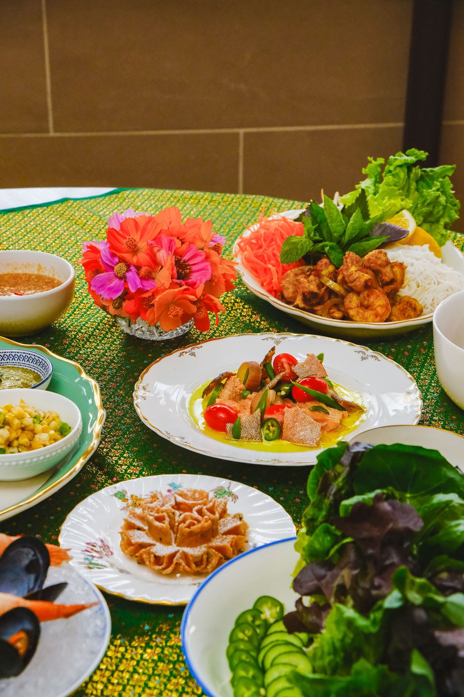 Colorful plates of Thai cuisine served with fresh flowers and garnishes on a green tablecloth.
