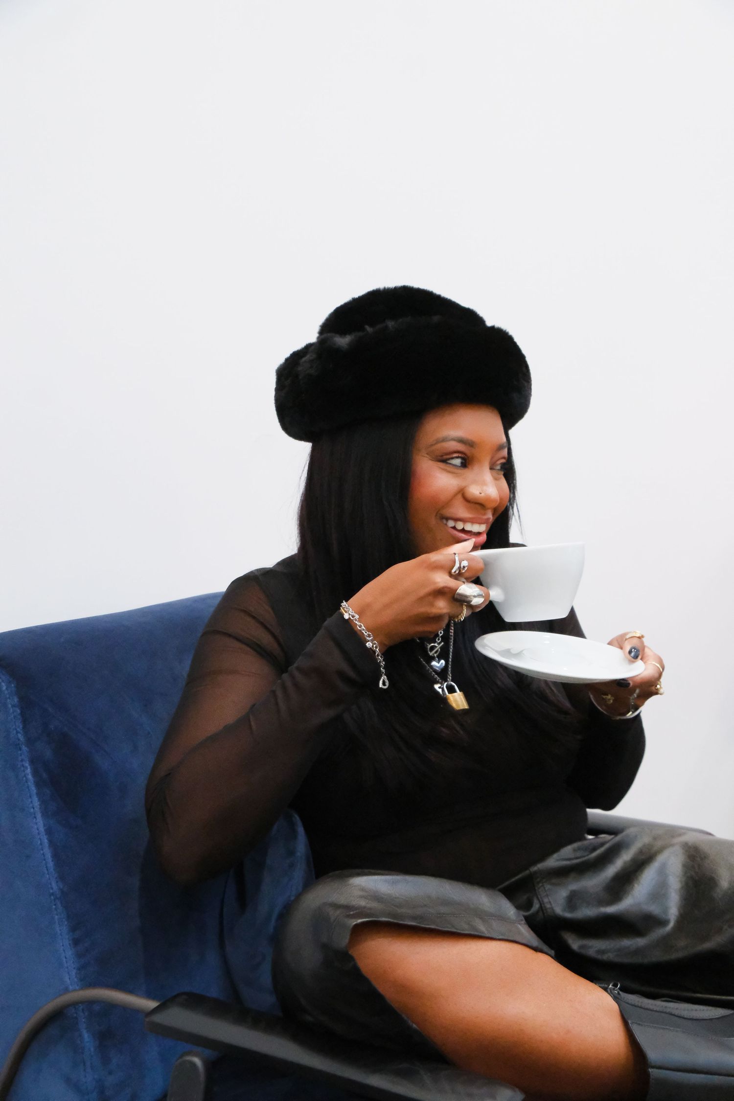 A person in black attire relaxes on a blue couch while sipping from a white teacup.