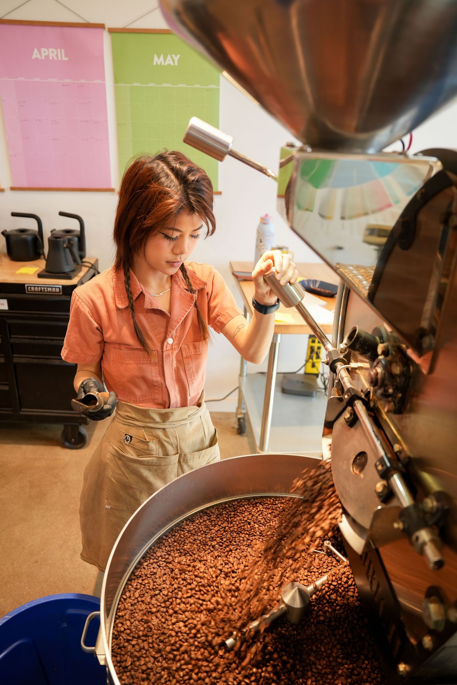 Woman operating a coffee roasting machine with fresh roasted beans in a professional roastery.