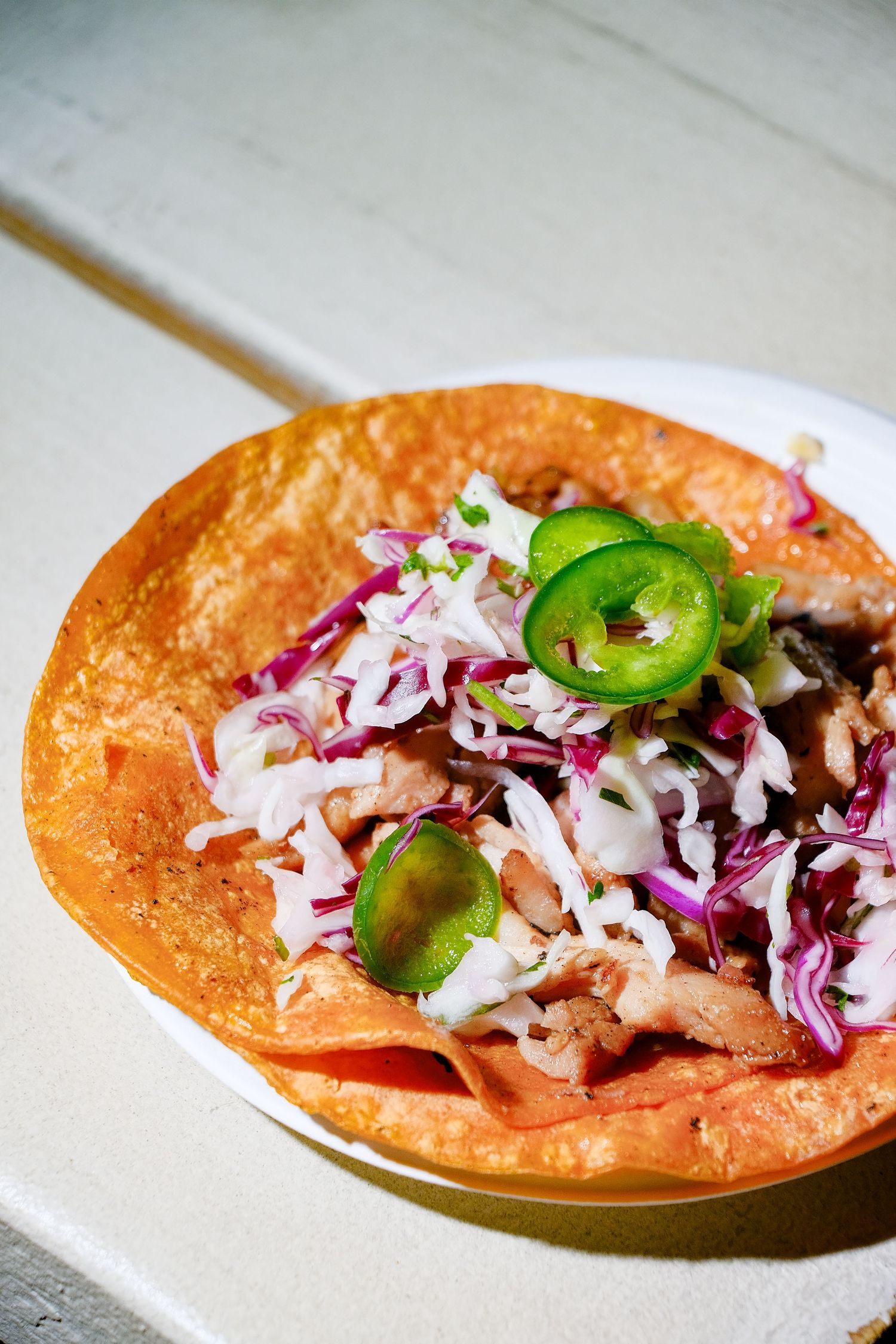A Mexican fish taco topped with shredded cabbage slaw and sliced jalapenos served on a bright orange tortilla.