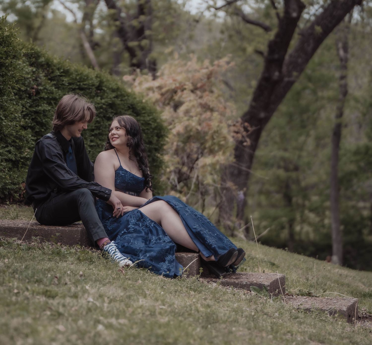 People relaxing on grassy hillside in natural wooded setting.