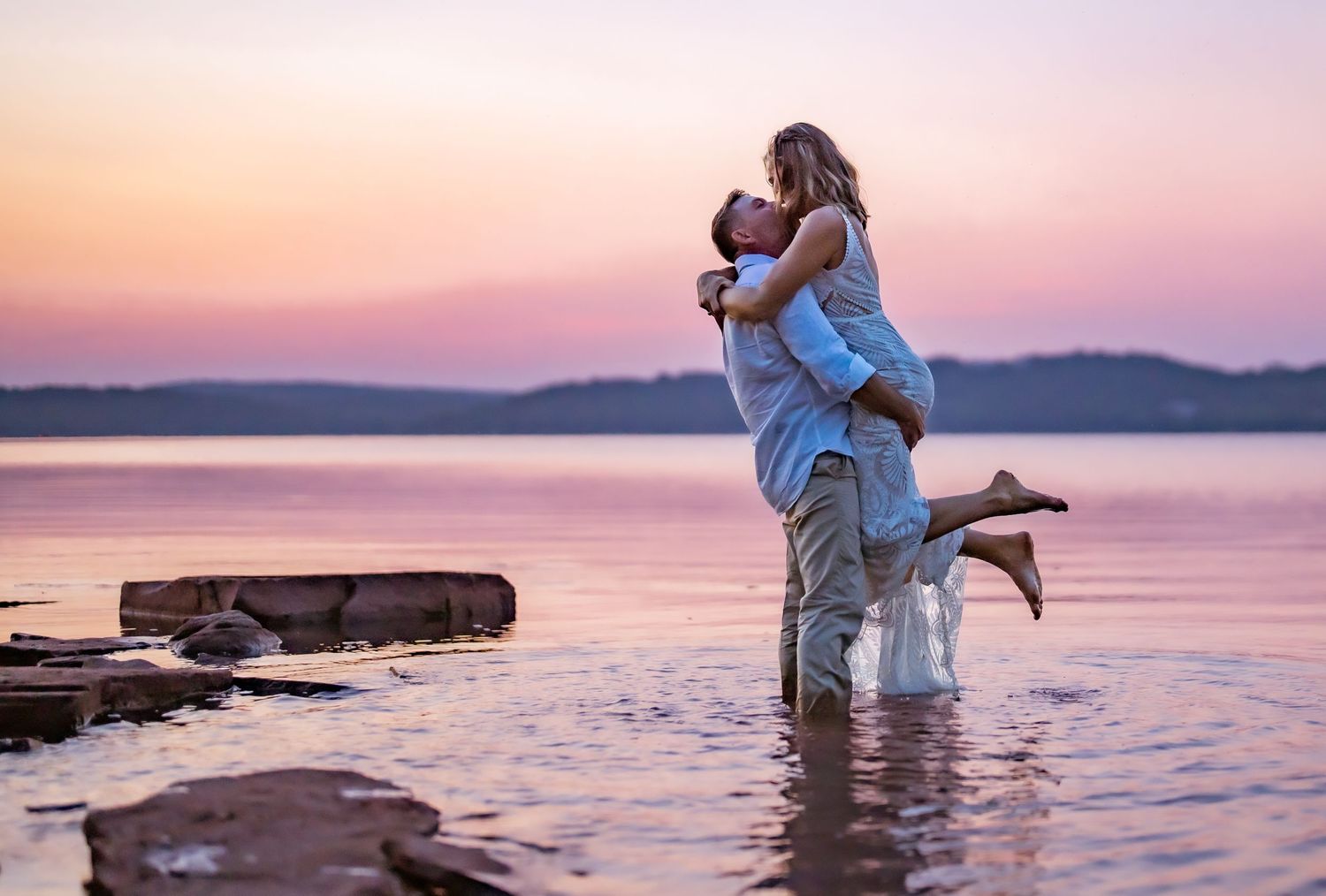 Romantic sunset photoshoot on rocky beach with water and mountains in background.