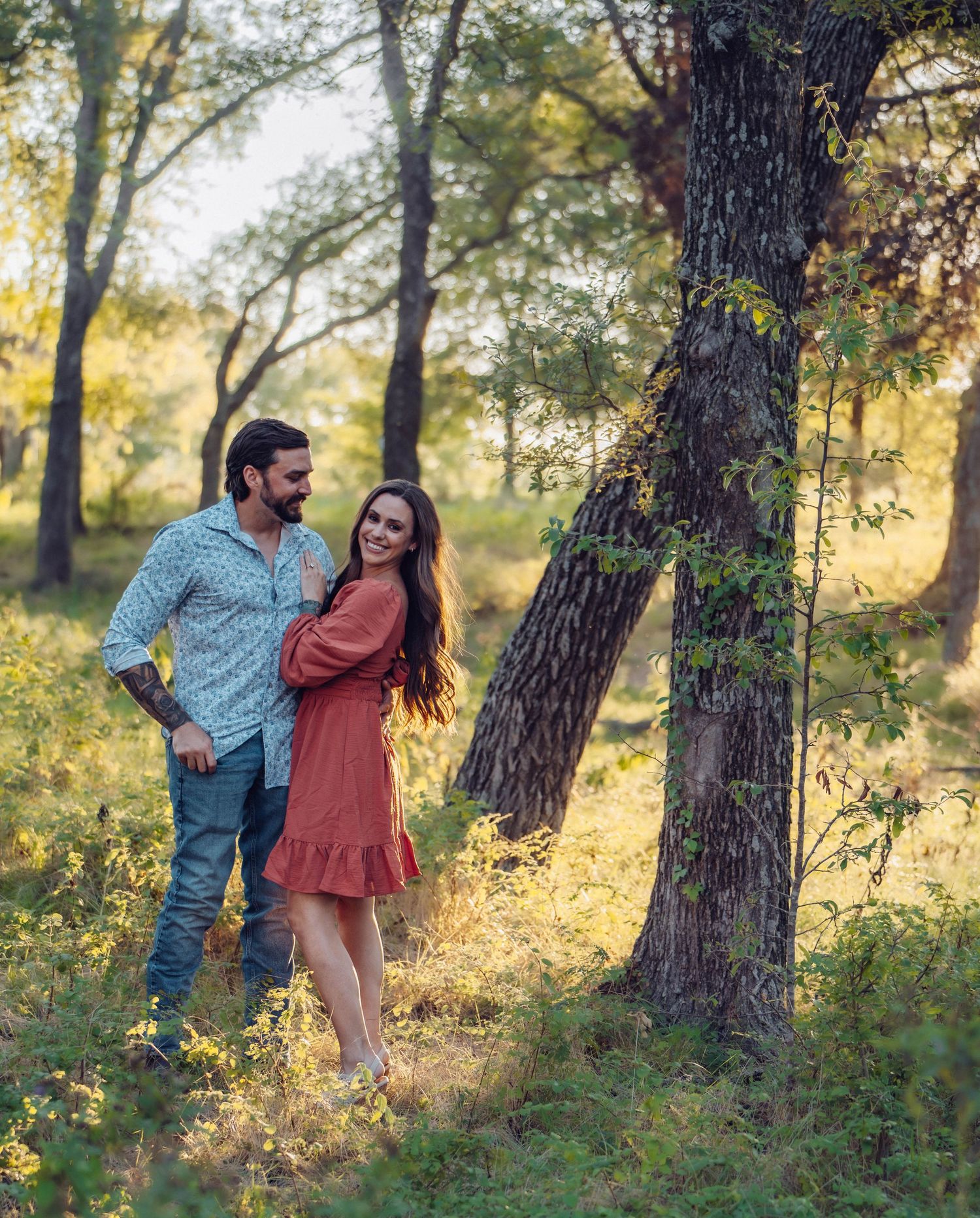 Romantic engagement photos taken in a golden sunlit forest setting.