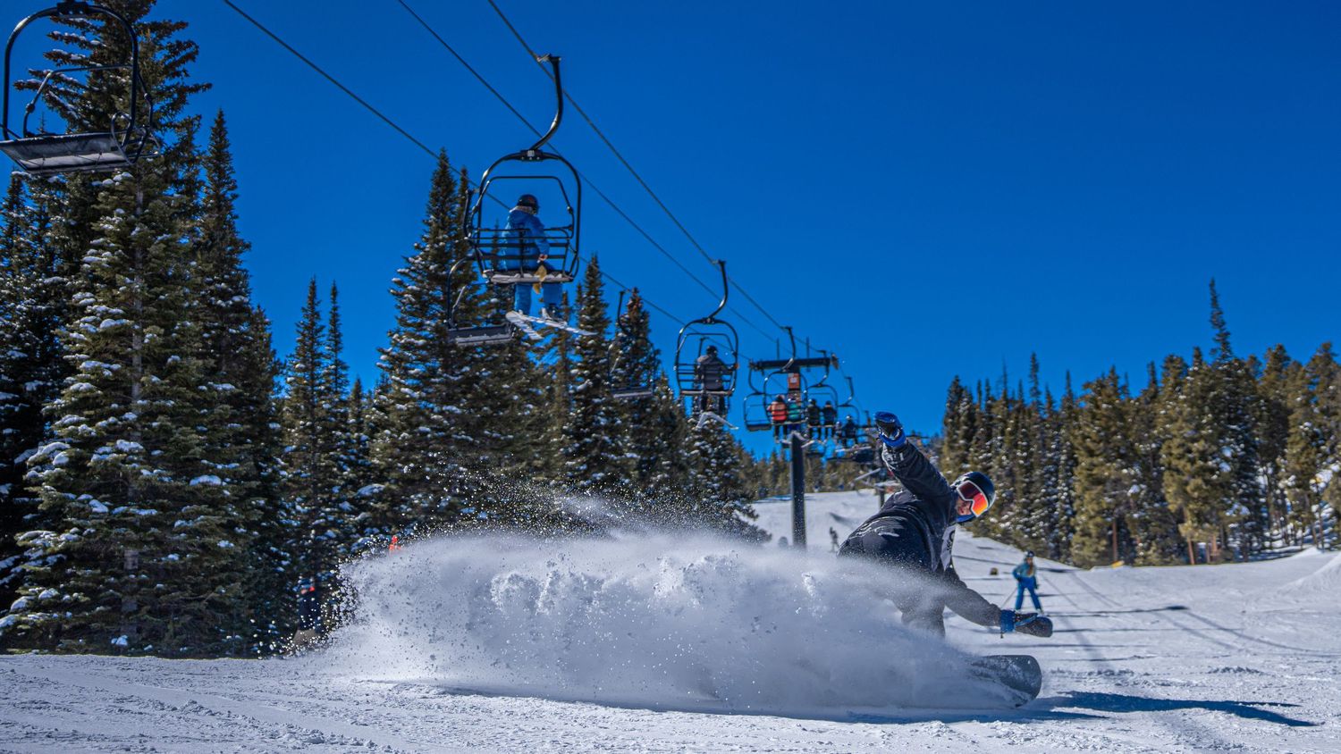 Snow boarder on a snow-covered ski resort landscape with chair lifts against bright blue sky.