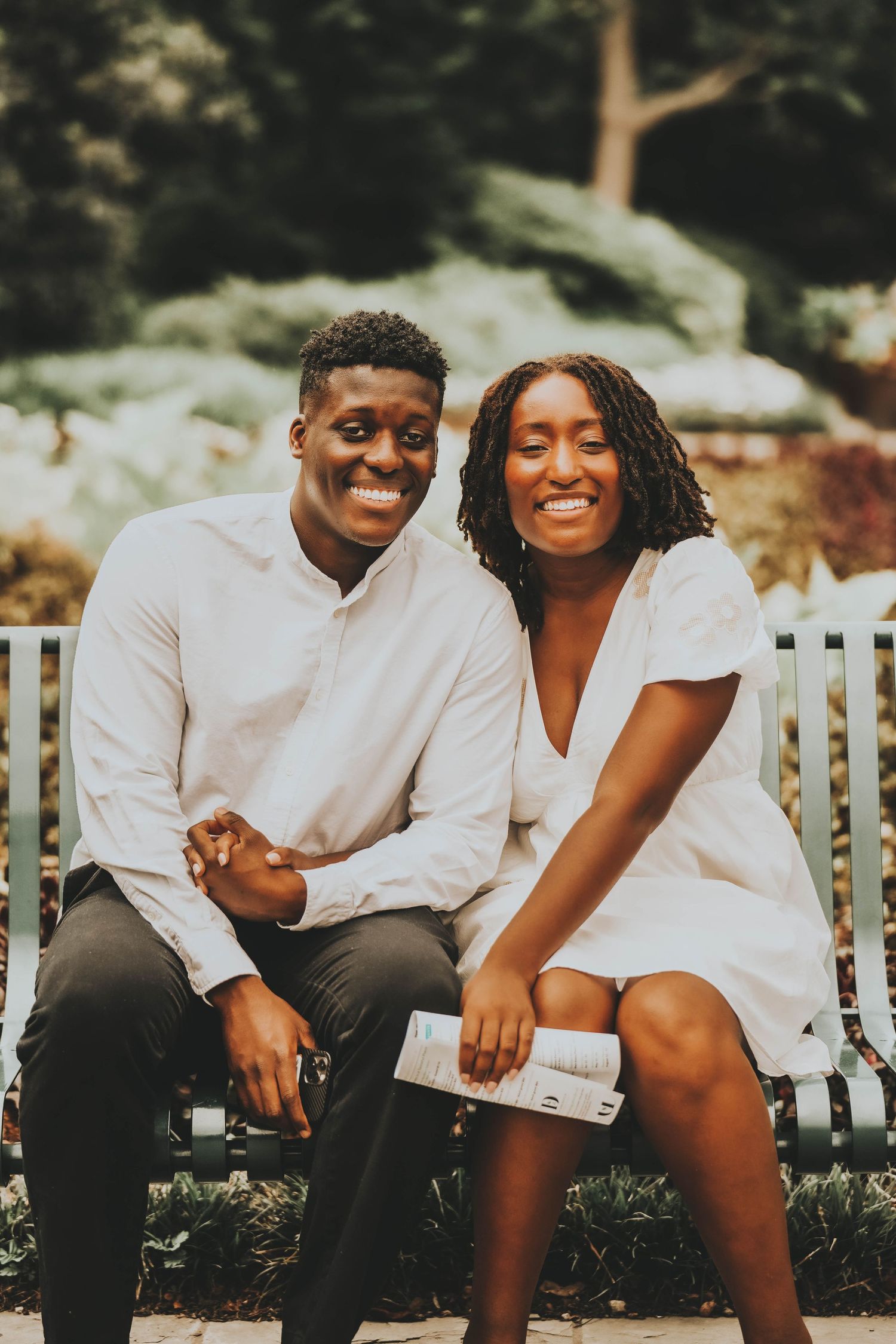 Couple in white clothing sharing candid moments on a garden bench outdoors.