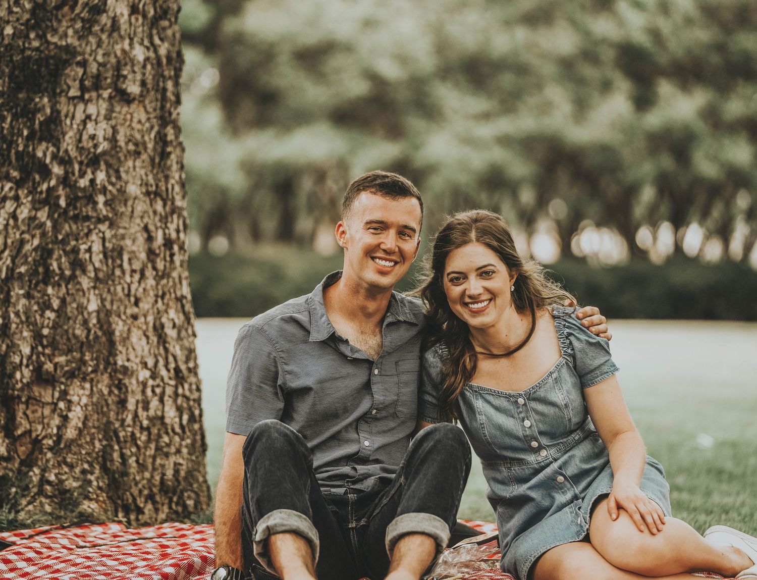 Couple relaxing outdoors on a picnic blanket under tall pine trees.