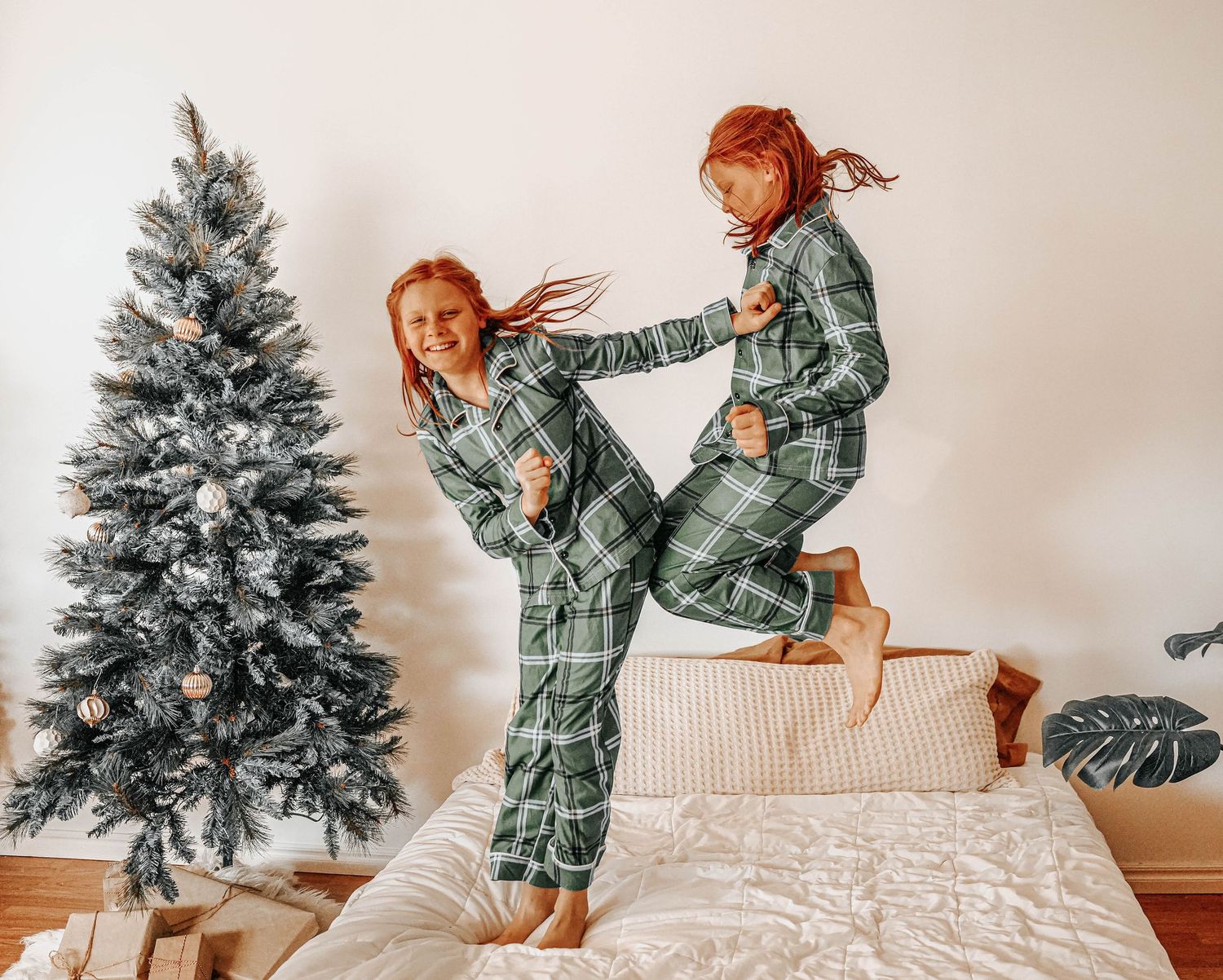 Playful holiday photos of people jumping on a white bed near a Christmas tree.