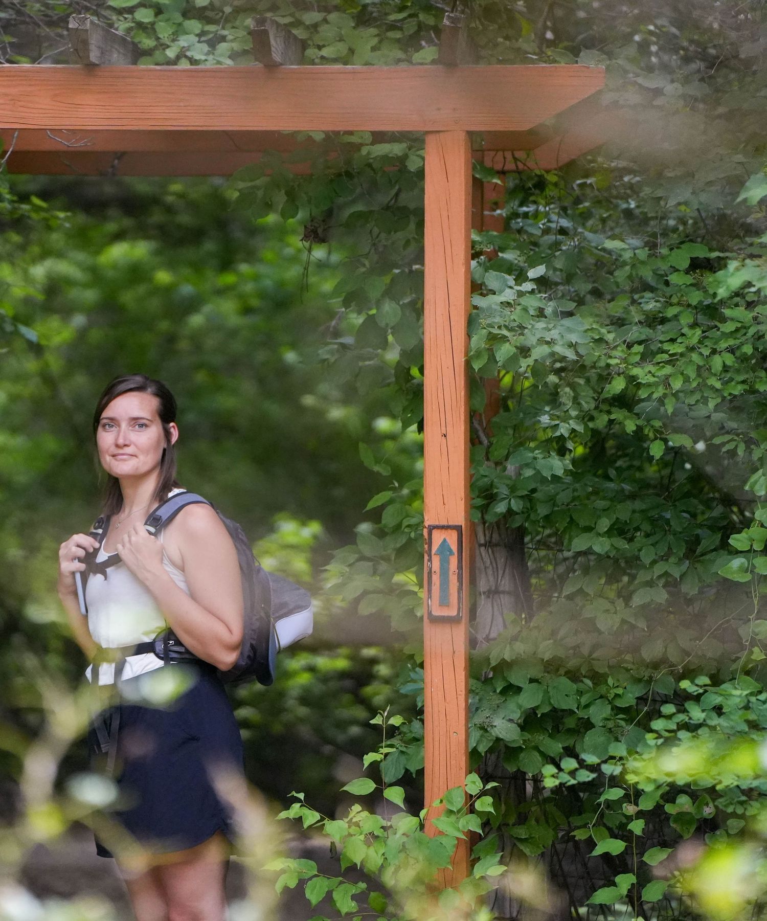 Outdoors under a wooden pergola surrounded by lush greenery in a garden setting.