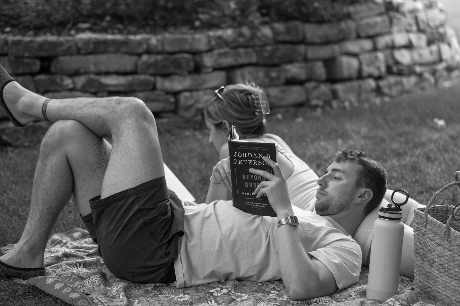 People reading on a blanket against an old stone wall on a sunny day.