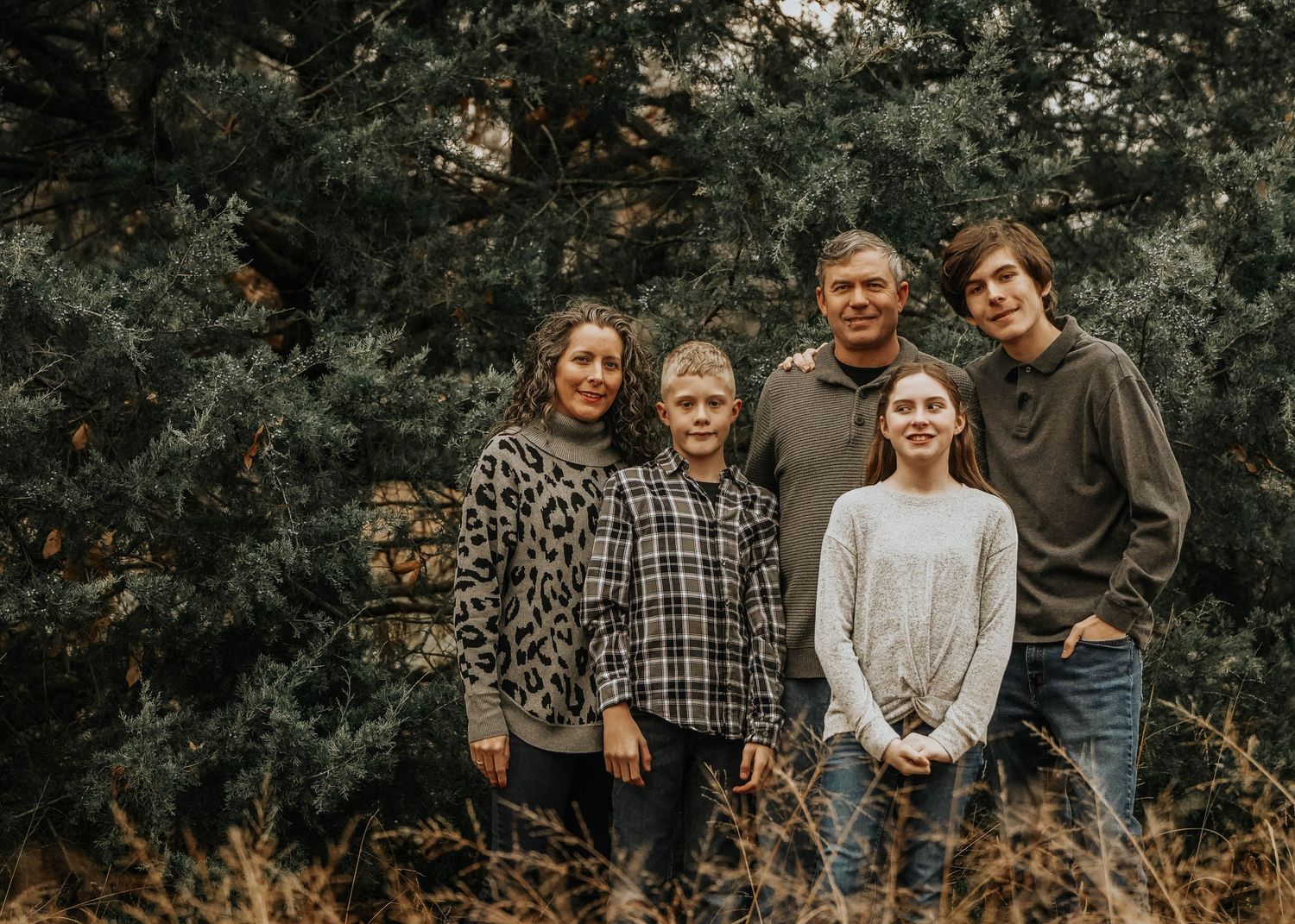 Casual family portrait in wooded area with fallen leaves and natural lighting.