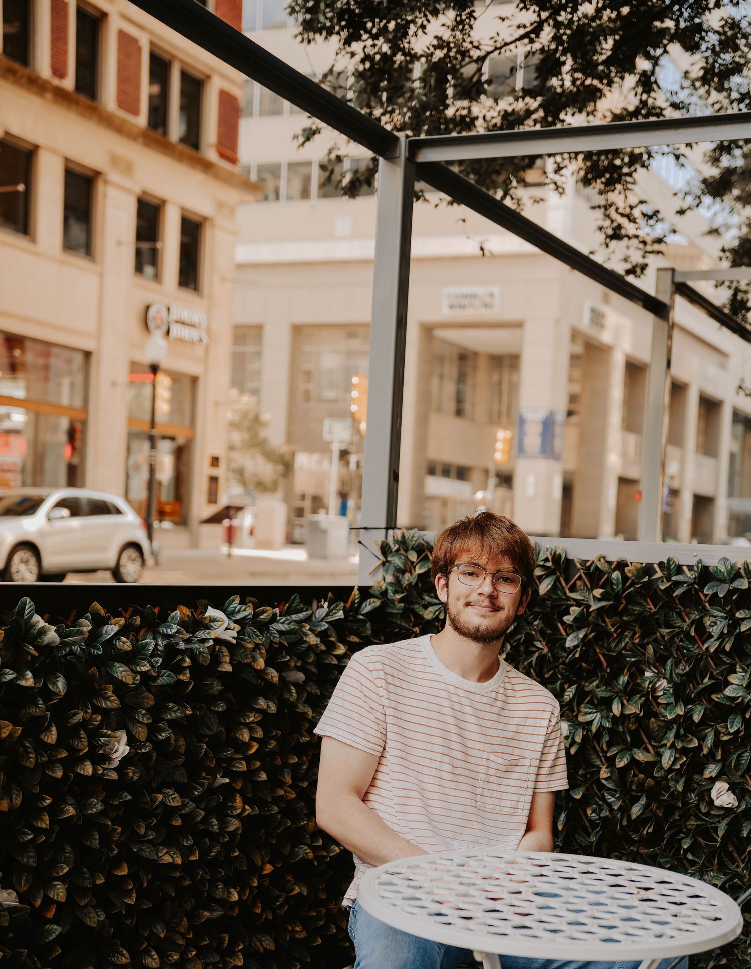 Outdoor cafe seating with striped shirt and casual attire against greenery wall.
