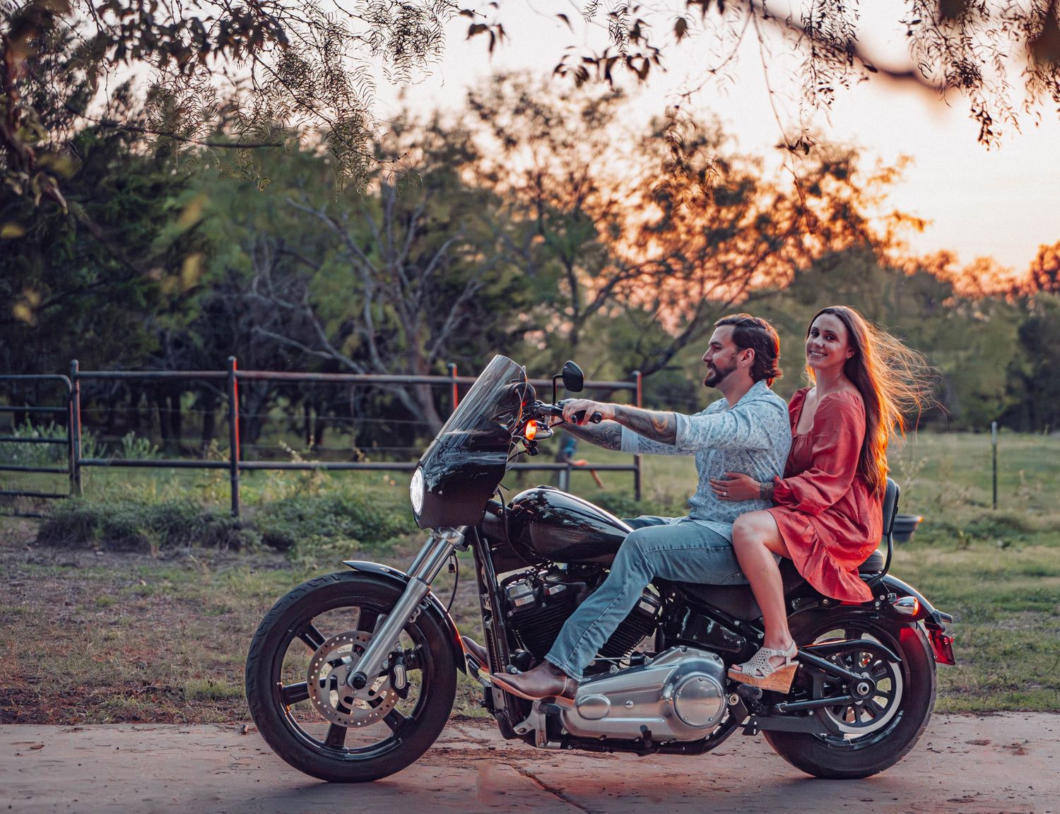 Romantic photoshoot featuring a vintage motorcycle at sunset in a rustic setting.