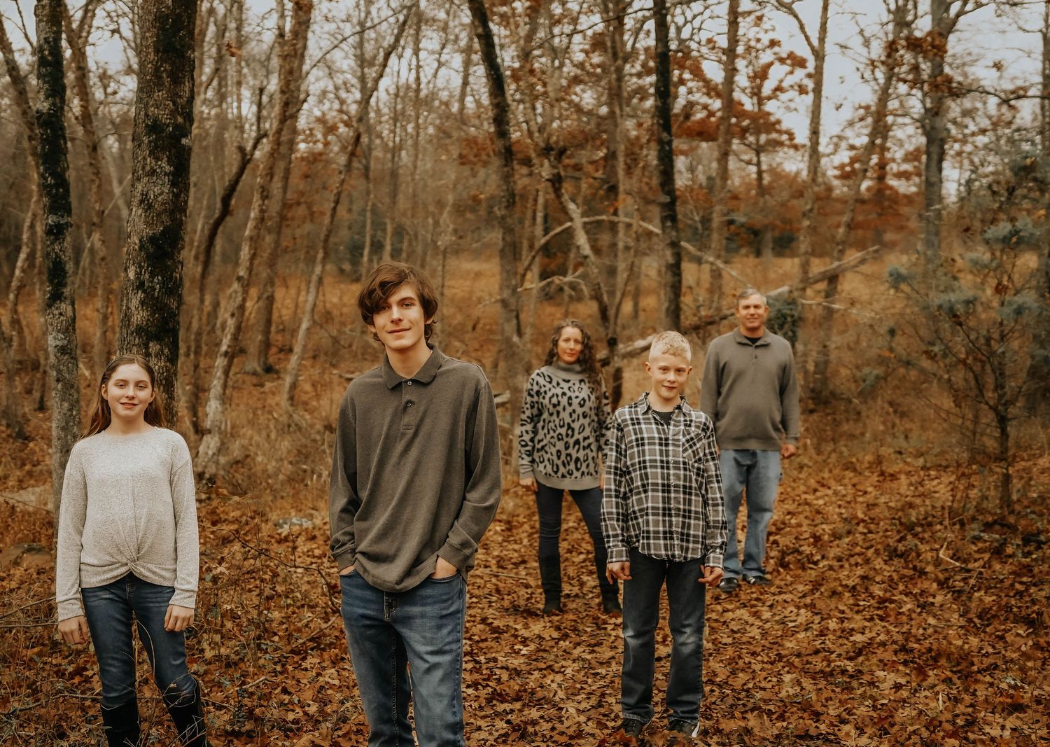 A group of people walking through autumn woods covered in fallen orange leaves.