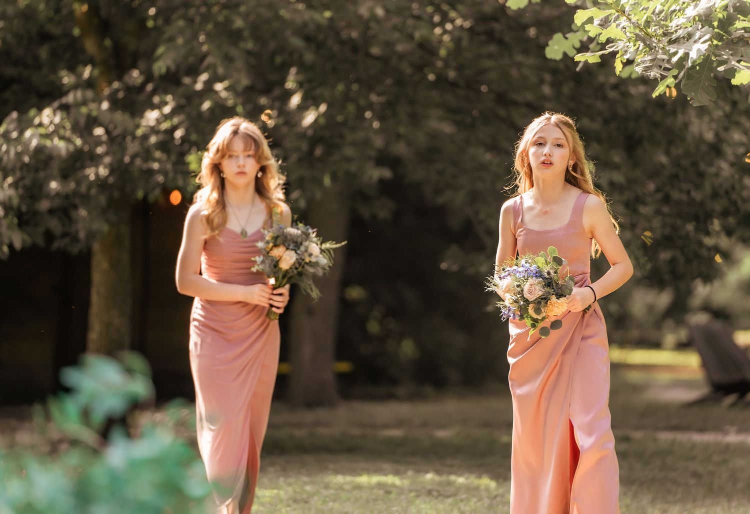 Bridesmaids wearing coral pink dresses pose together during an outdoor wedding.
