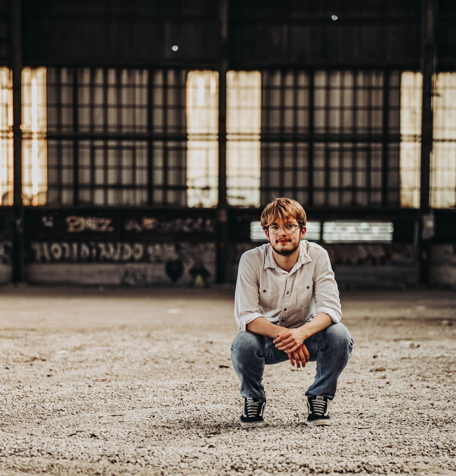 Person in casual attire sitting on rough concrete ground in an industrial space.