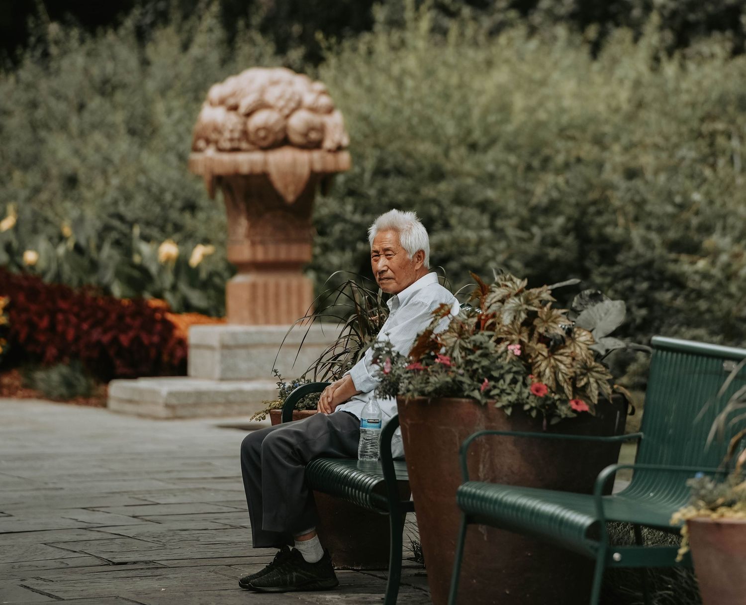 Garden setting resting on a park bench surrounded by potted plants.
