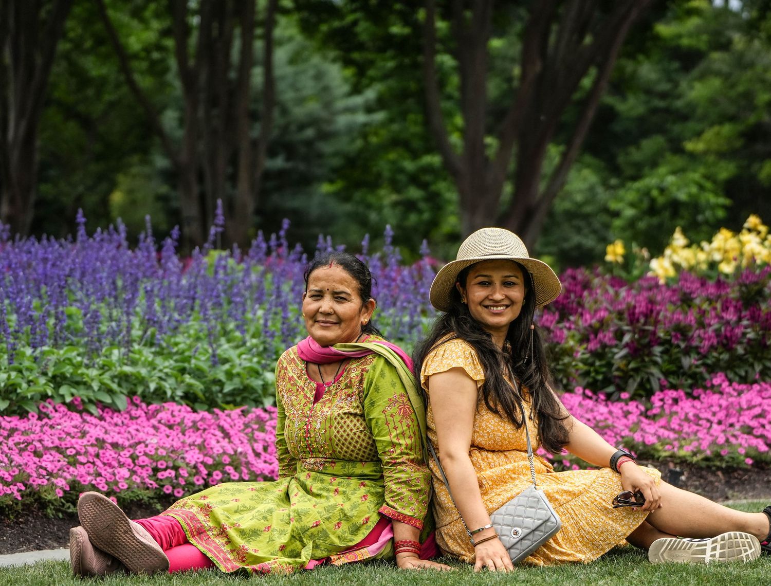 Two people lounging in a colorful flower garden with purple and pink blooms.