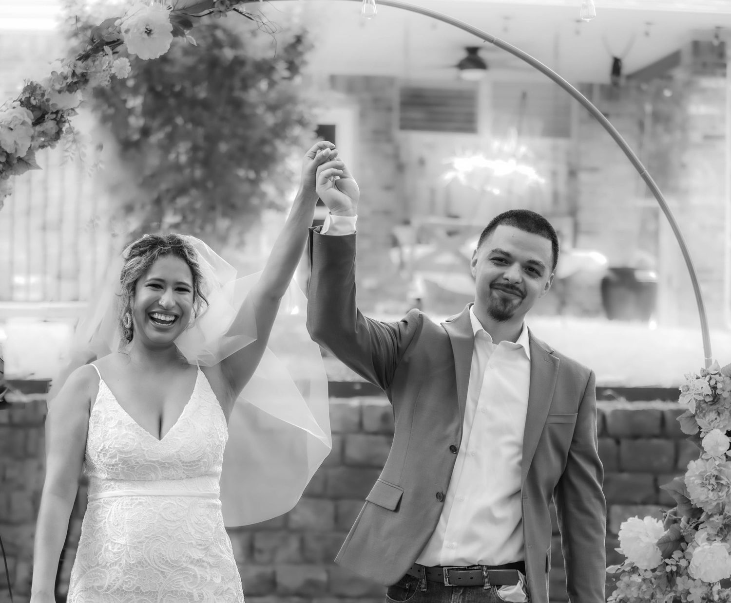 Black and white wedding portrait showing joyful celebration under an archway.