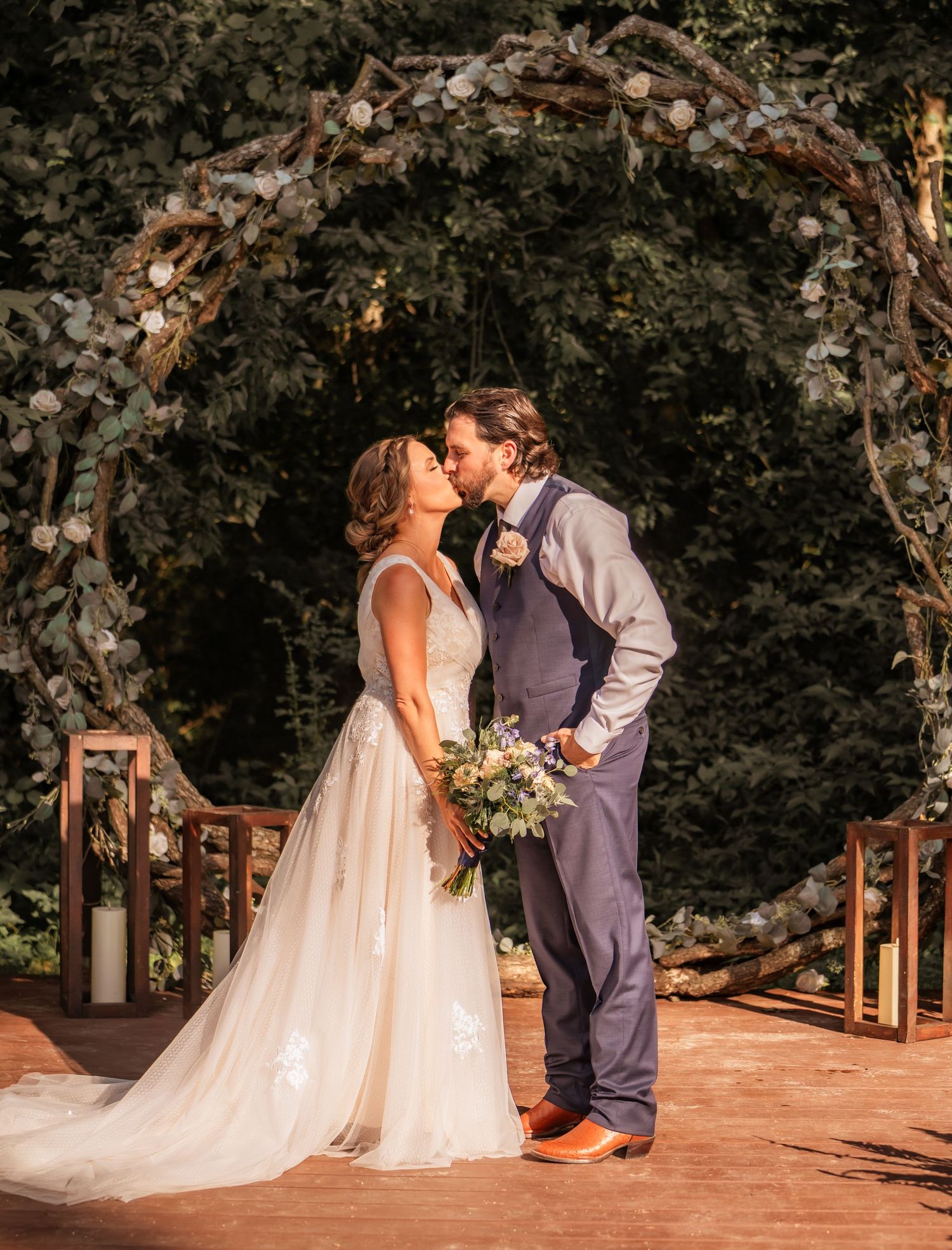 Romantic outdoor wedding ceremony under flowering trees with wooden chairs and candle decorations.