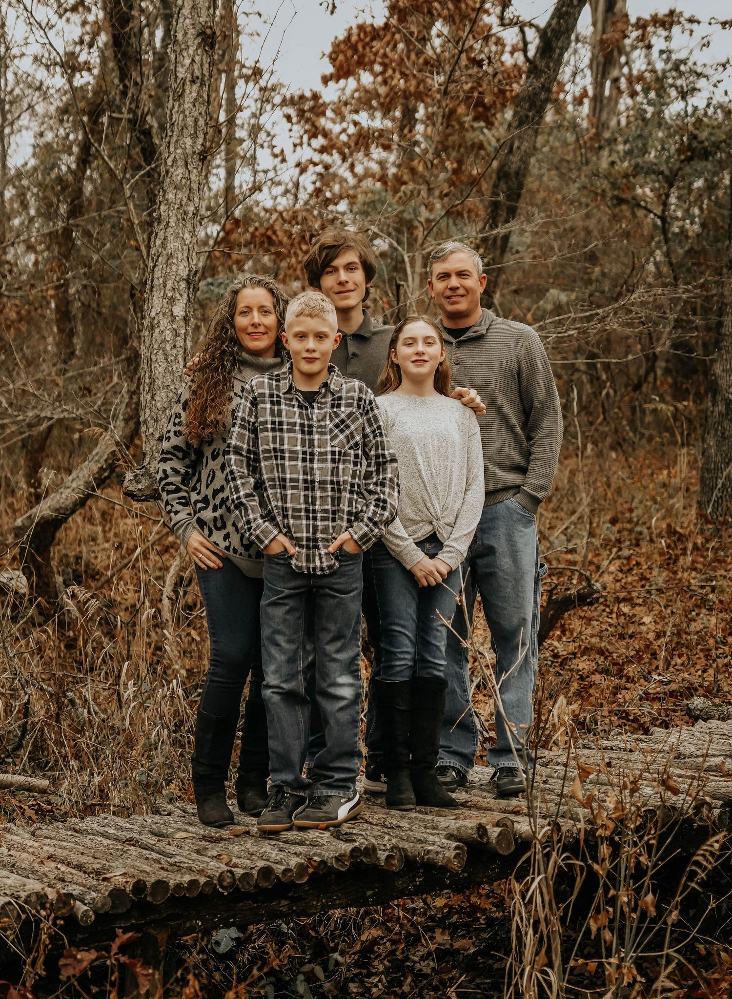 Family group posing on fallen log in autumn woodland setting.
