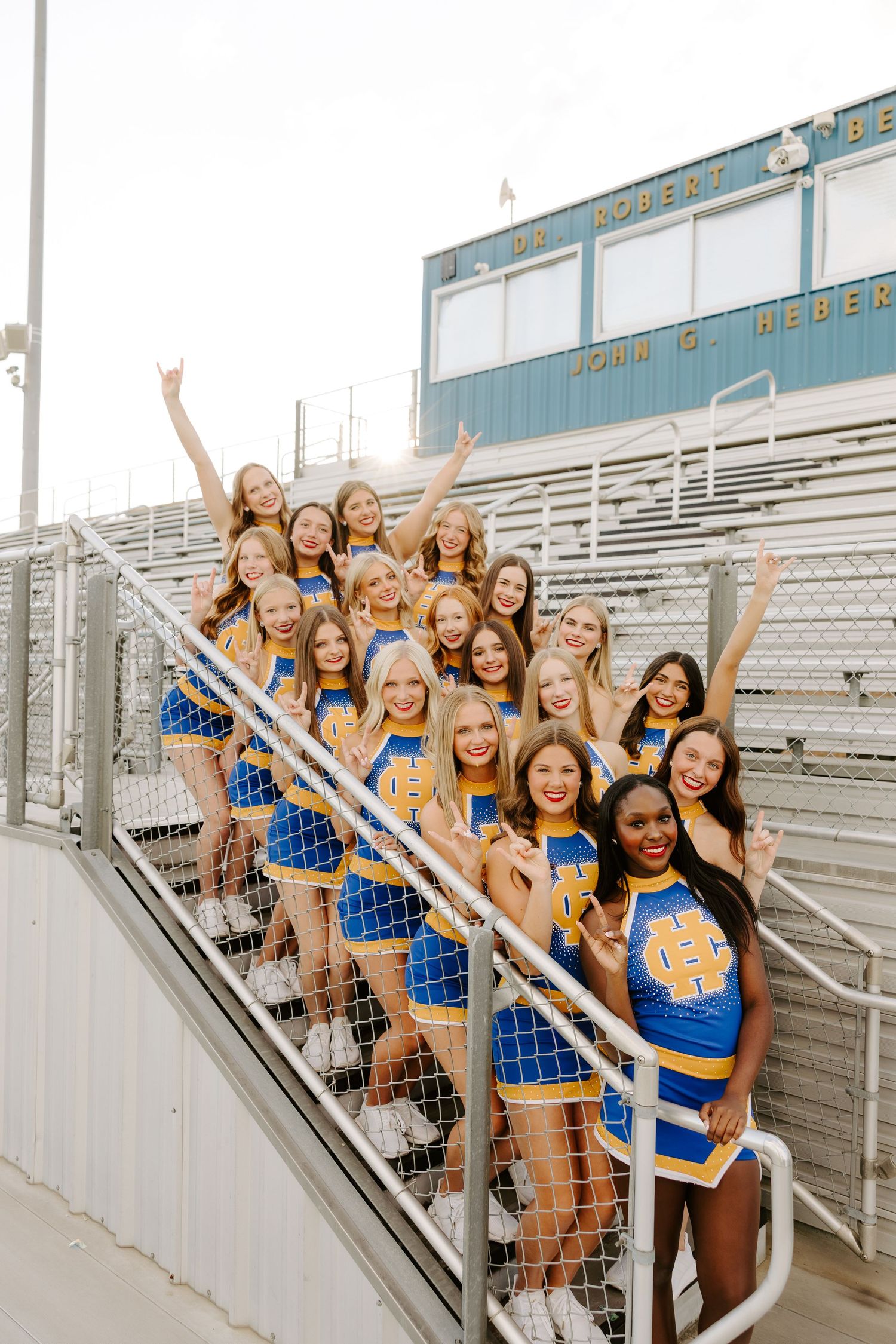 Henry Clay high school cheerleading squad posing on stadium bleacher stairs in blue and gold uniforms.