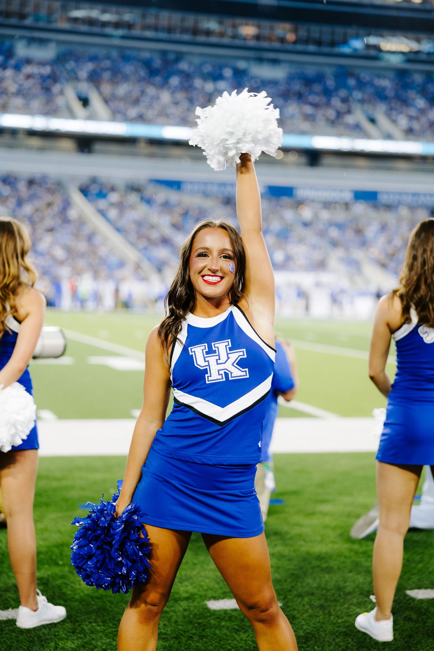 A cheerleader in a blue University of Kentucky uniform performs with pom poms during a football game.