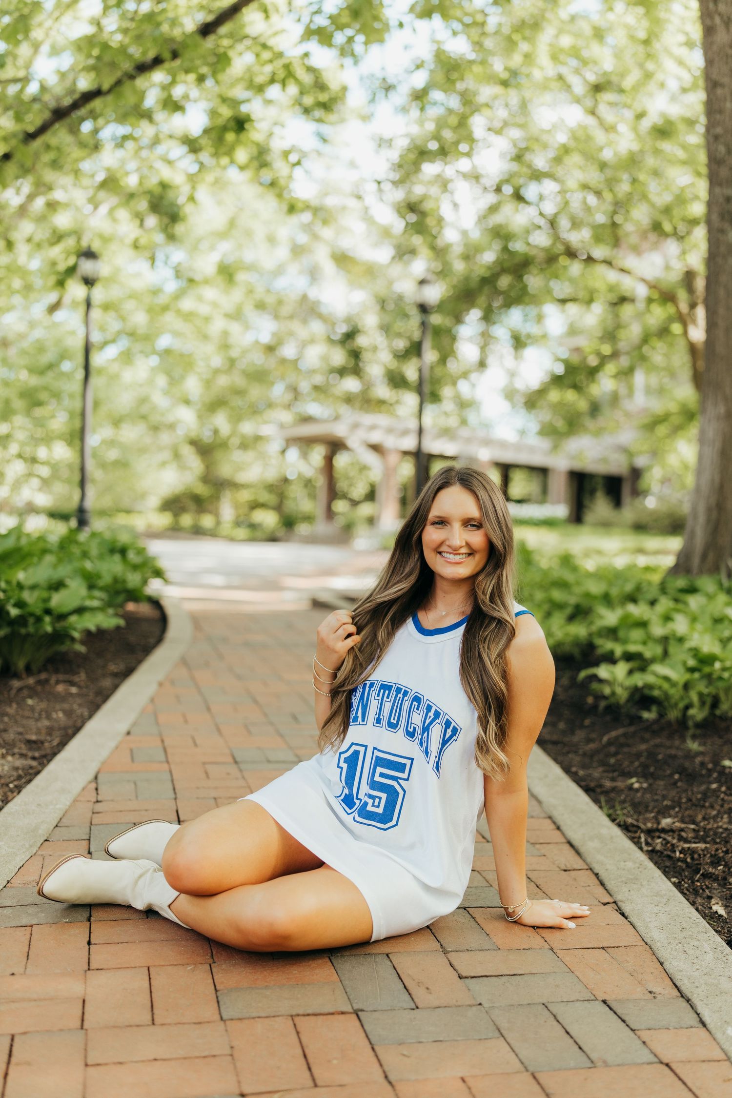Student in Kentucky sports jersey poses on brick pathway surrounded by greenery.
