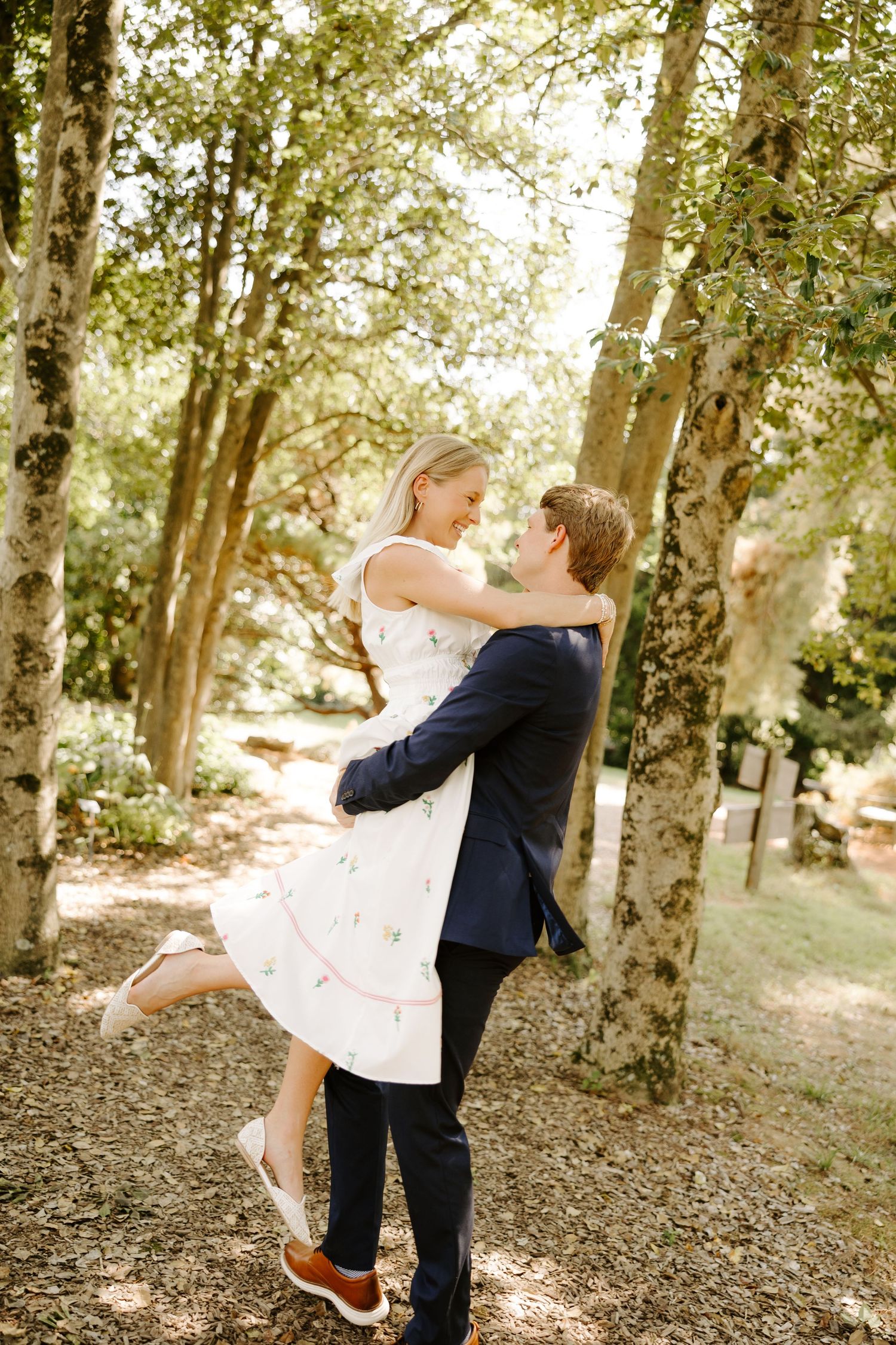 Playful couple dancing and embracing in a serene forest environment.