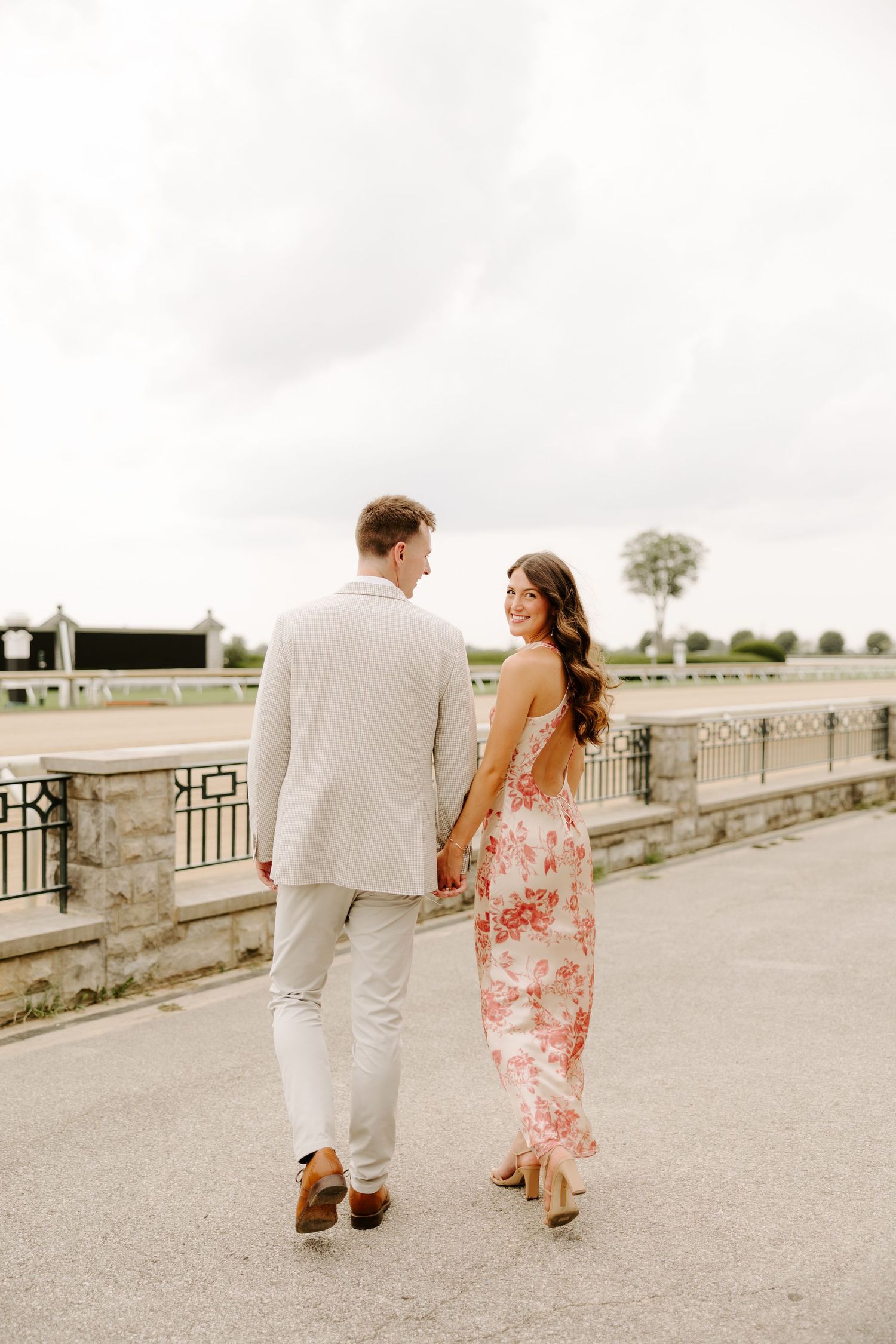 Couple walking hand in hand away from camera on a promenade, woman glancing back with a smile.