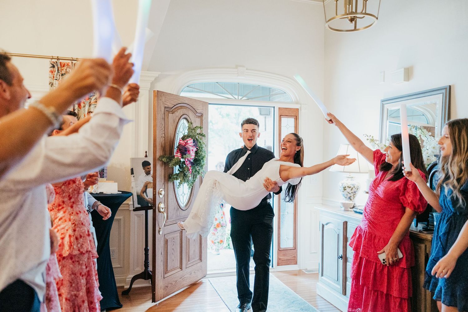 Wedding guests wave ribbons as bride and groom enter reception through elegant arched doorway.
