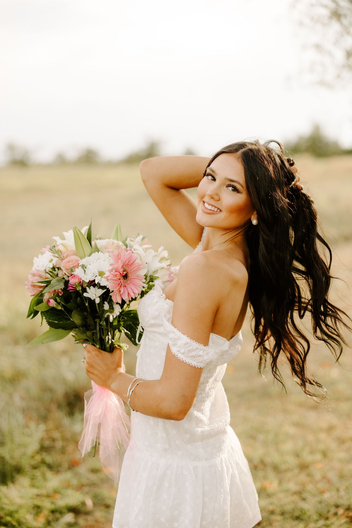 A joyful outdoor portrait with a pink and white bouquet against a natural backdrop.