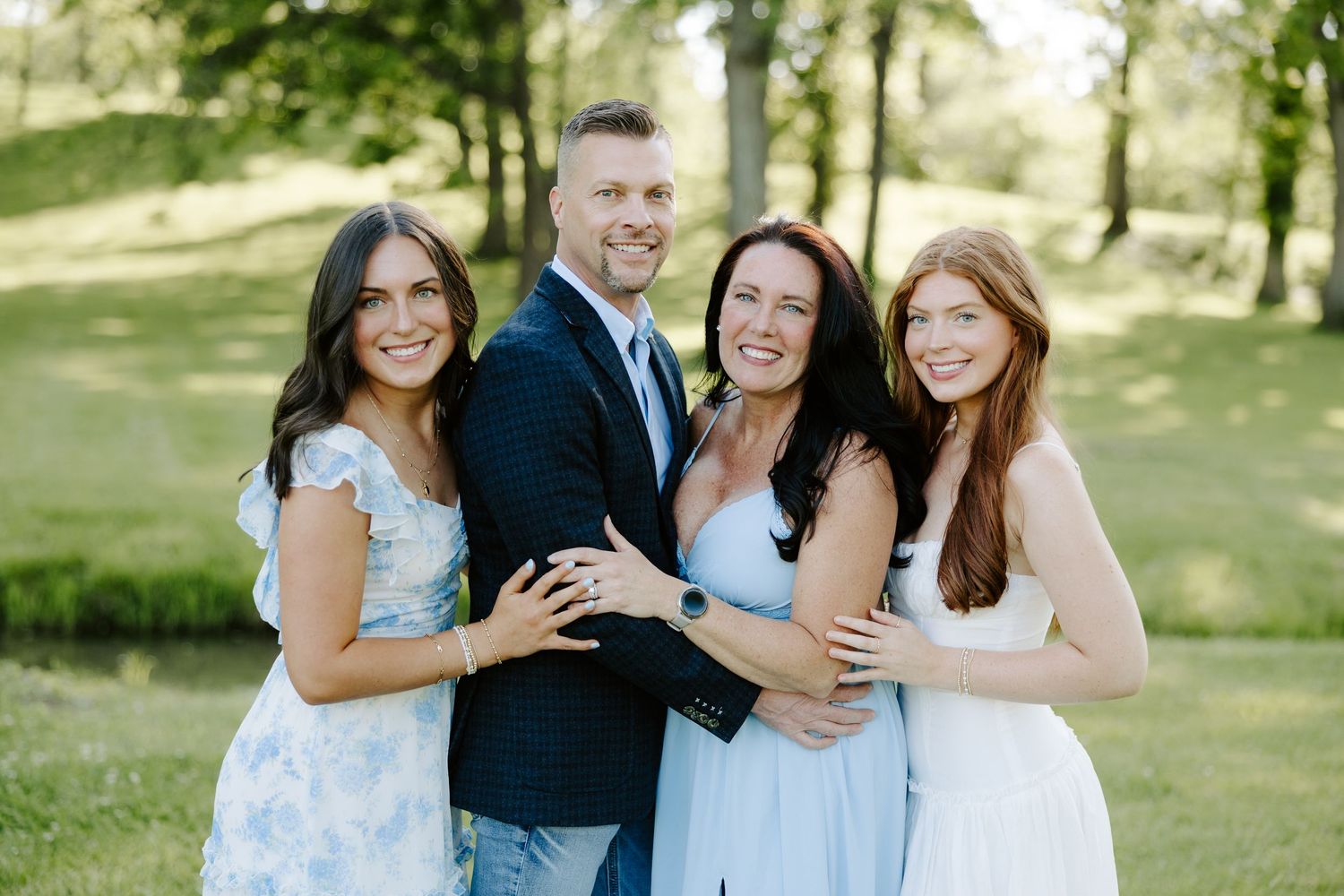 A smiling group of four people pose together outdoors on a green lawn in summer attire.