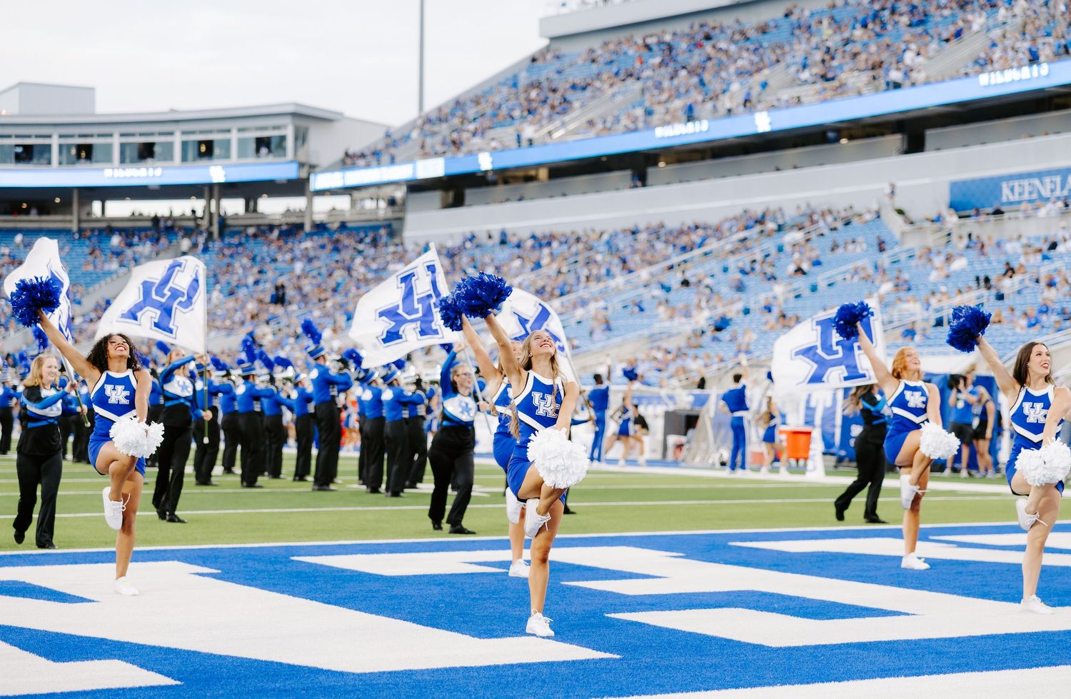 University of Kentucky cheerleaders wave flags and perform on the blue turf during a Wildcats home football game.