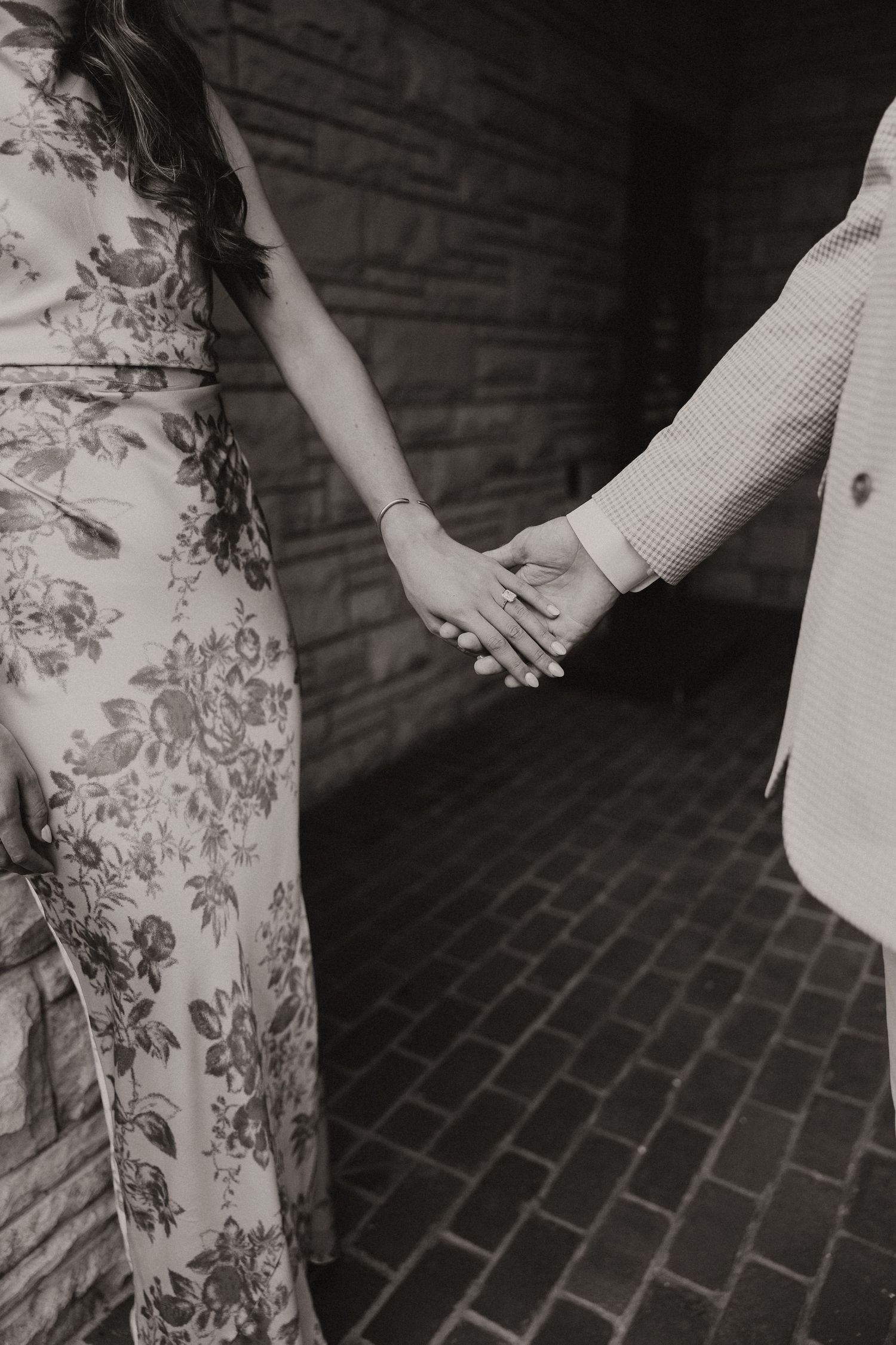 Close-up black and white photo of an engaged couple holding hands, showcasing a diamond engagement ring.