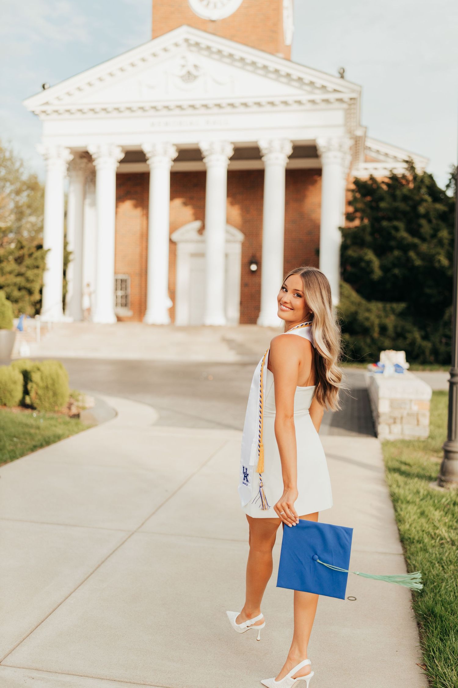 Graduate holds blue diploma while standing in front of classic university building with columns.