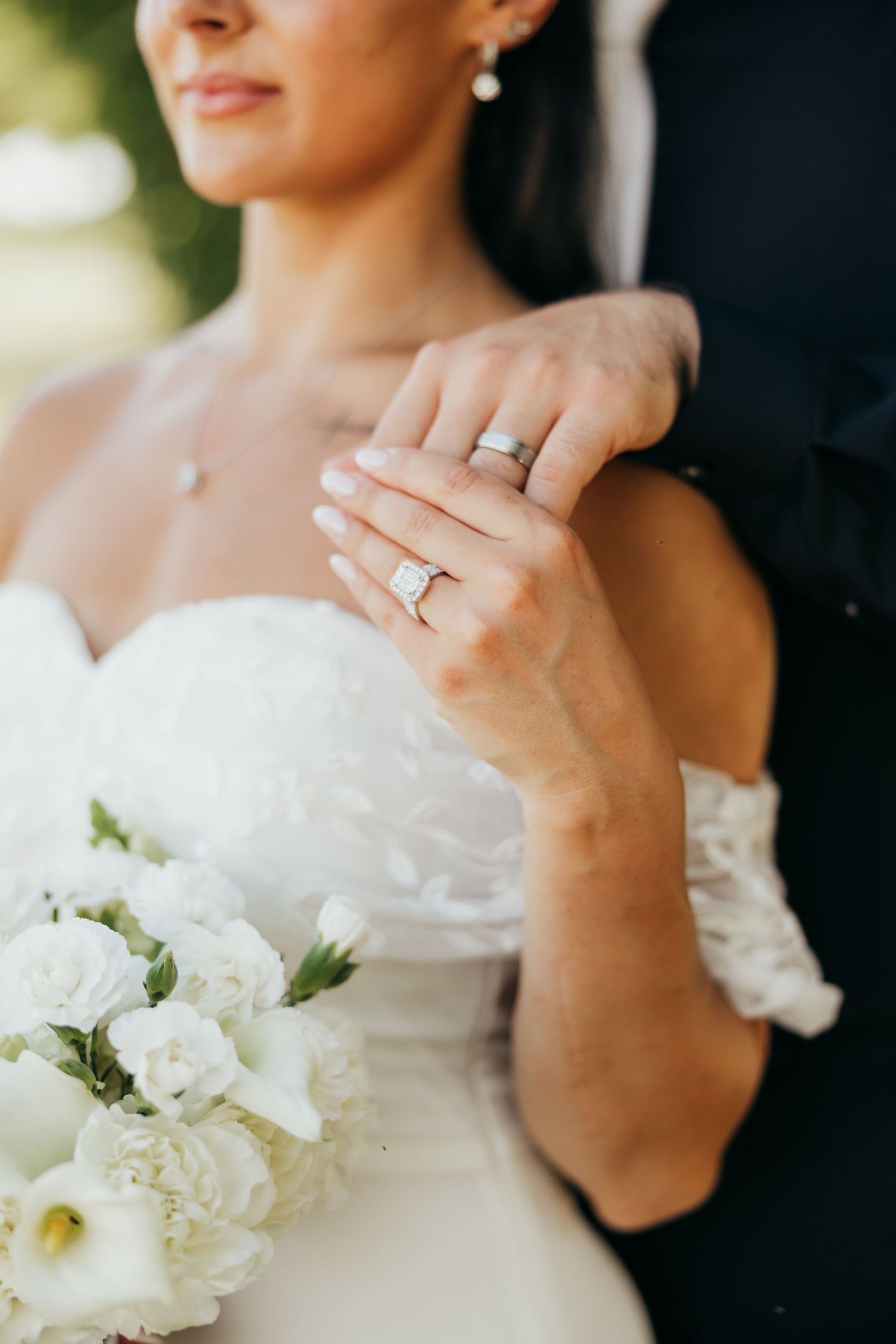 Bride displaying stunning diamond engagement ring and wedding band while holding white floral bouquet.