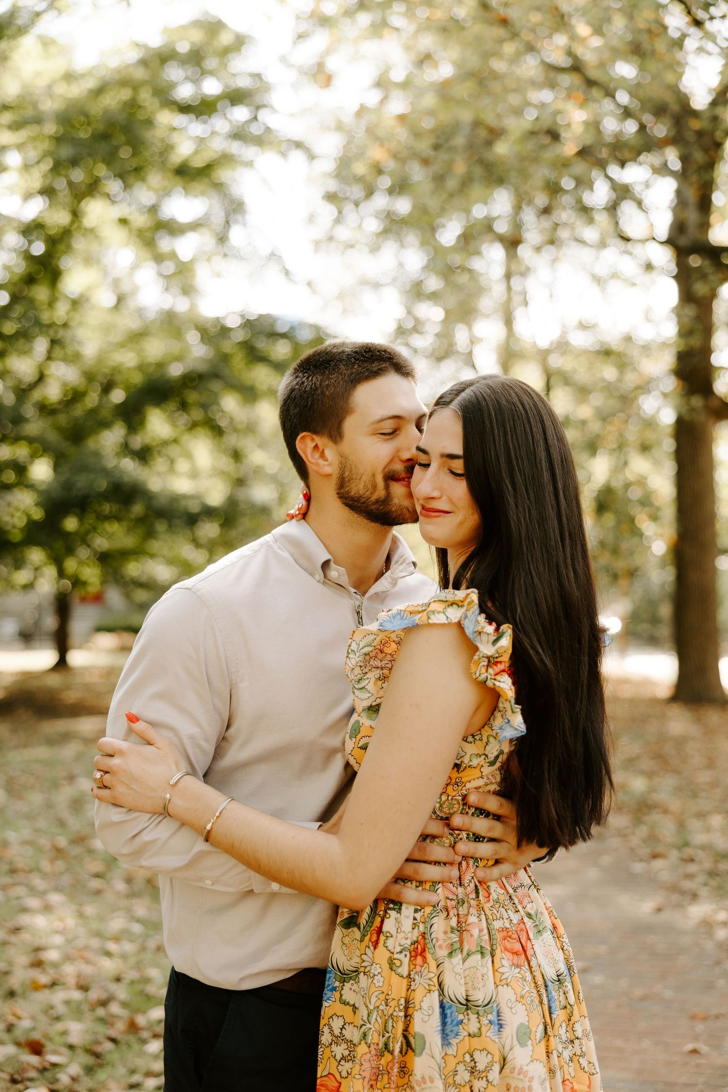 Couple embracing in autumn park, woman in floral dress leaning into mans gentle kiss.