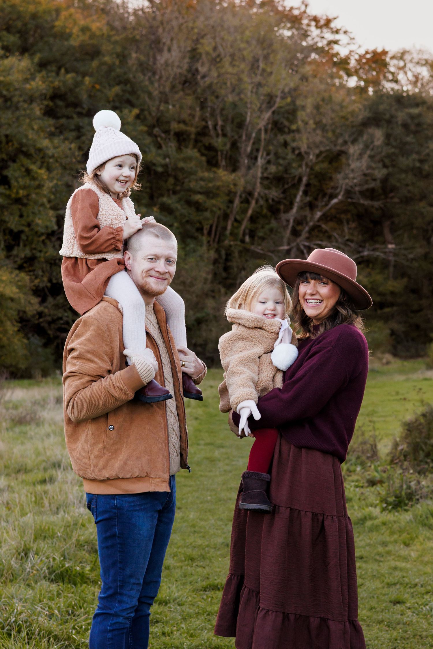 A family enjoys an autumn day outdoors together in a field with trees in the background.