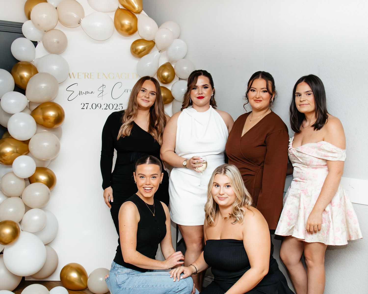 A group poses together against a white and gold balloon backdrop for a celebratory photoshoot.
