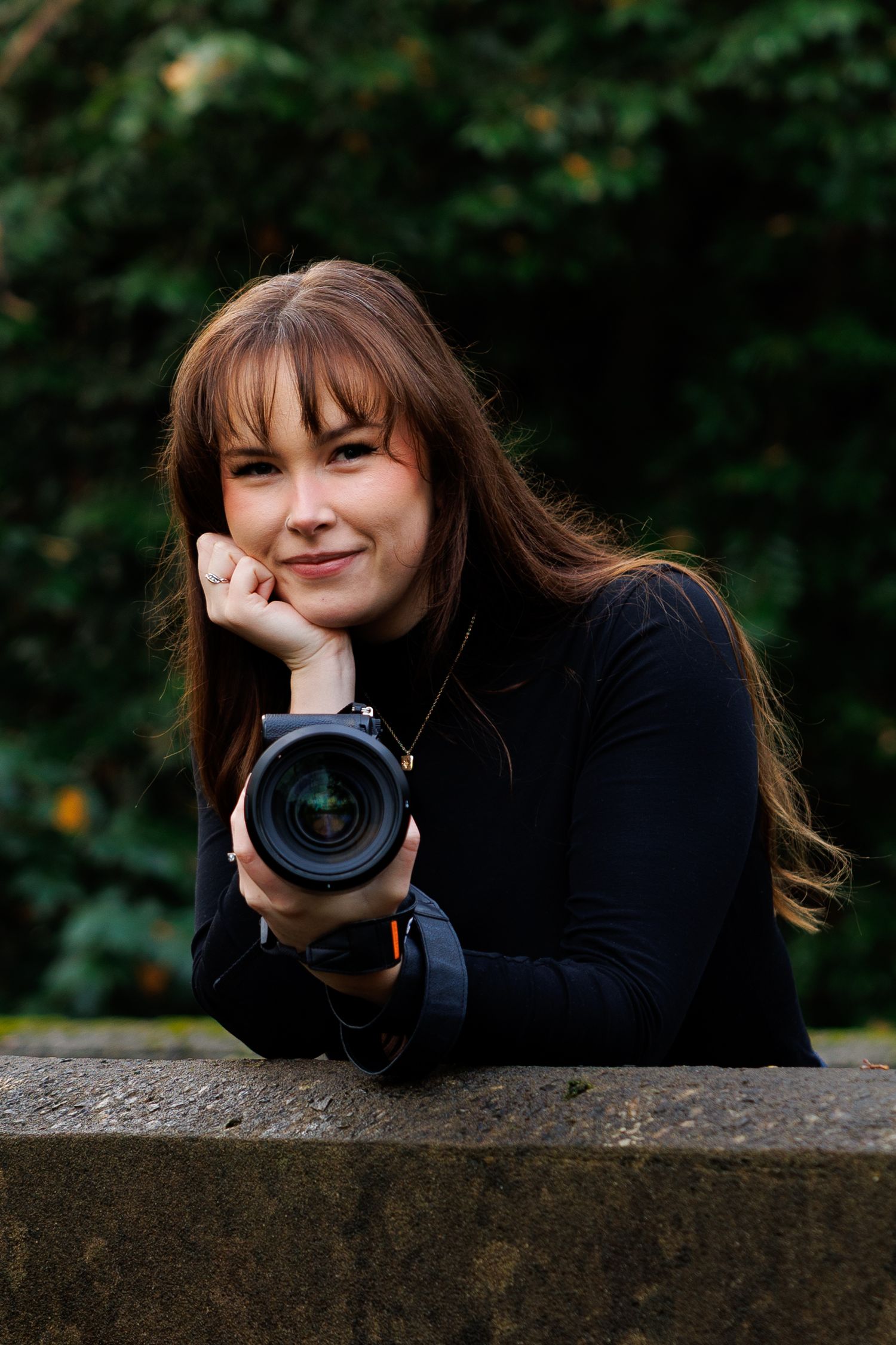 A photographer with long hair lies on a stone wall while holding a professional camera in a series of candid poses.