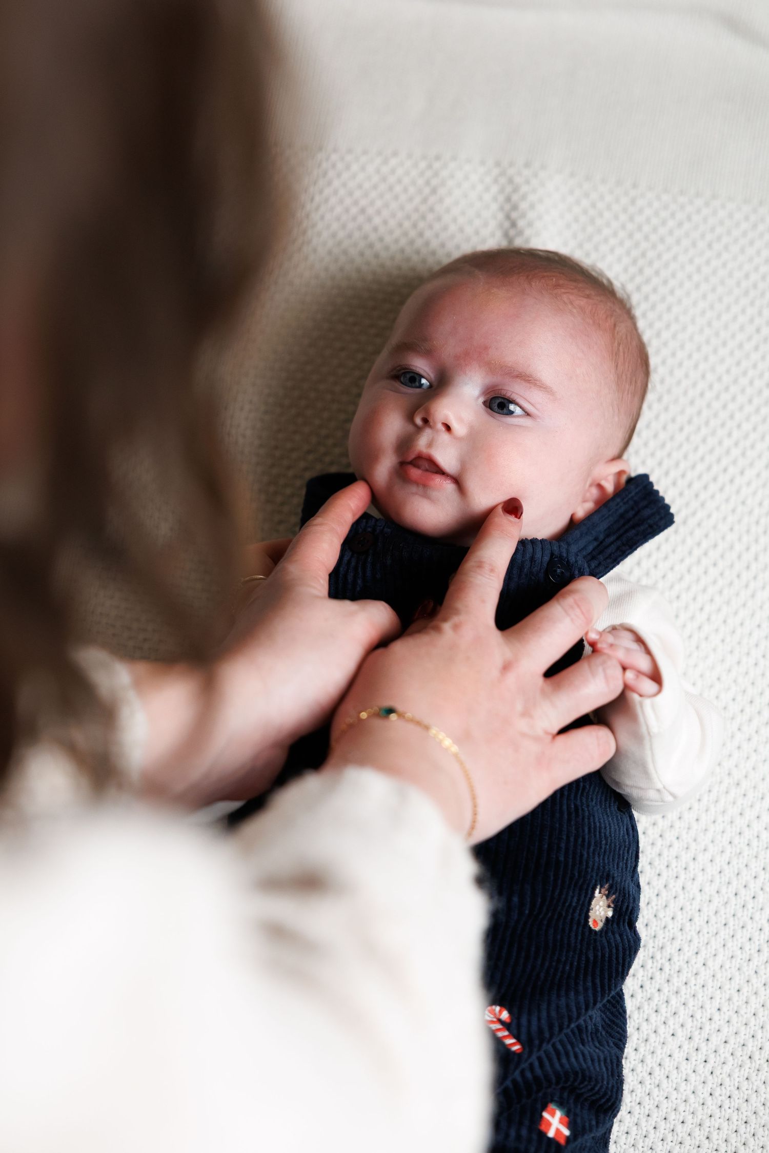 Baby lying on white textured surface wearing navy knit sweater in a sequence of close-up shots.