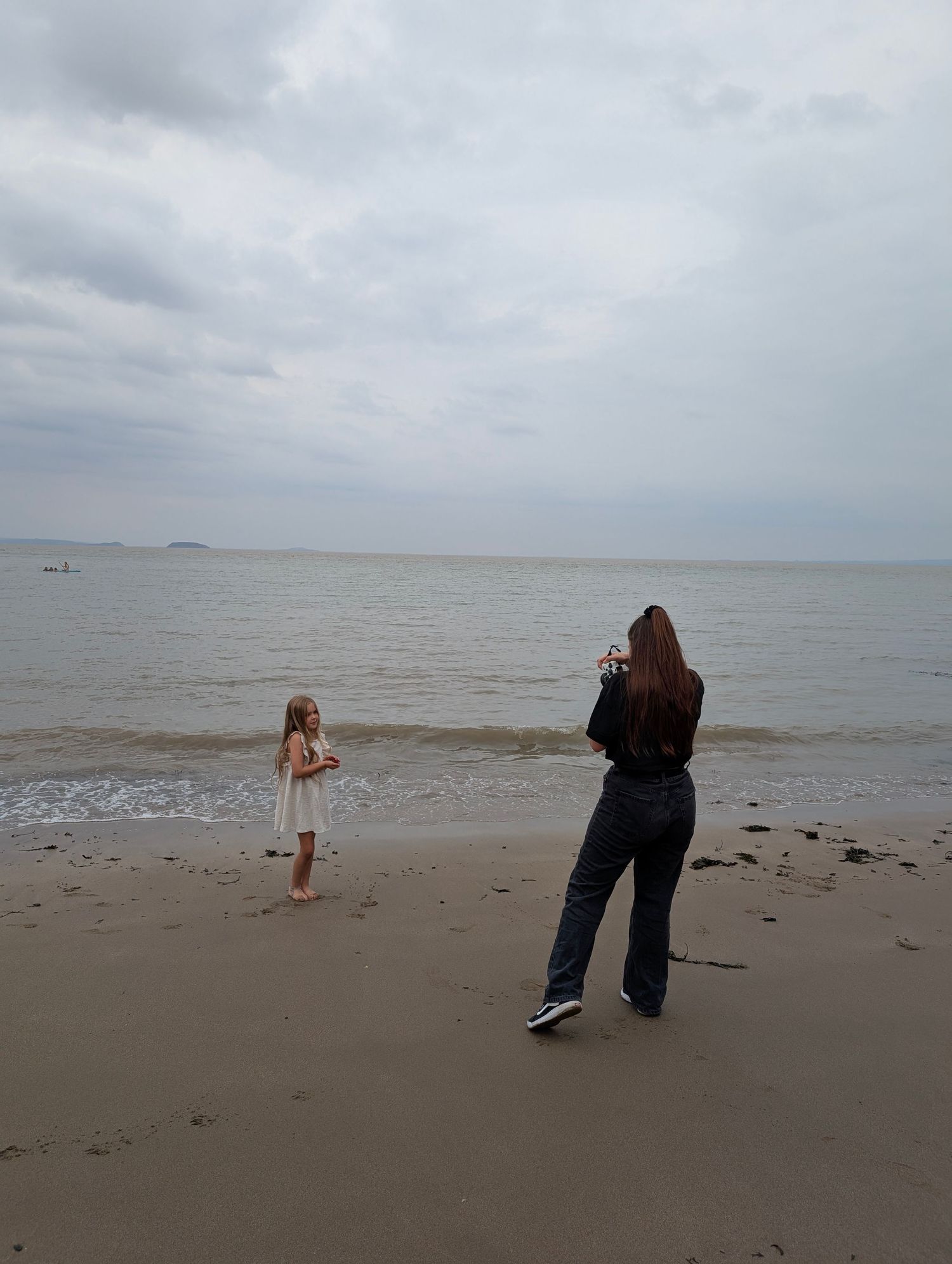 A collection of people taking photos with a phone at different angles on an overcast beach by the ocean.